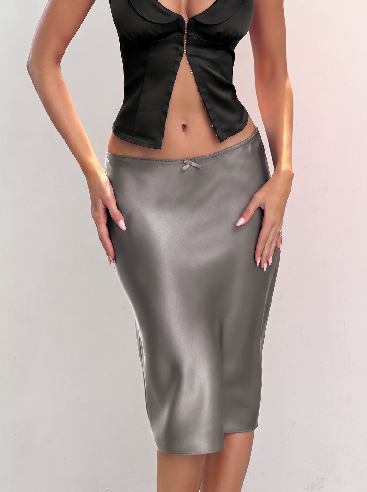 The ASPEN MIDI SKIRT - CHARCOAL is a charcoal grey bias-cut satin midi skirt with a 90s-inspired column silhouette and a small bow at the center front waistband.