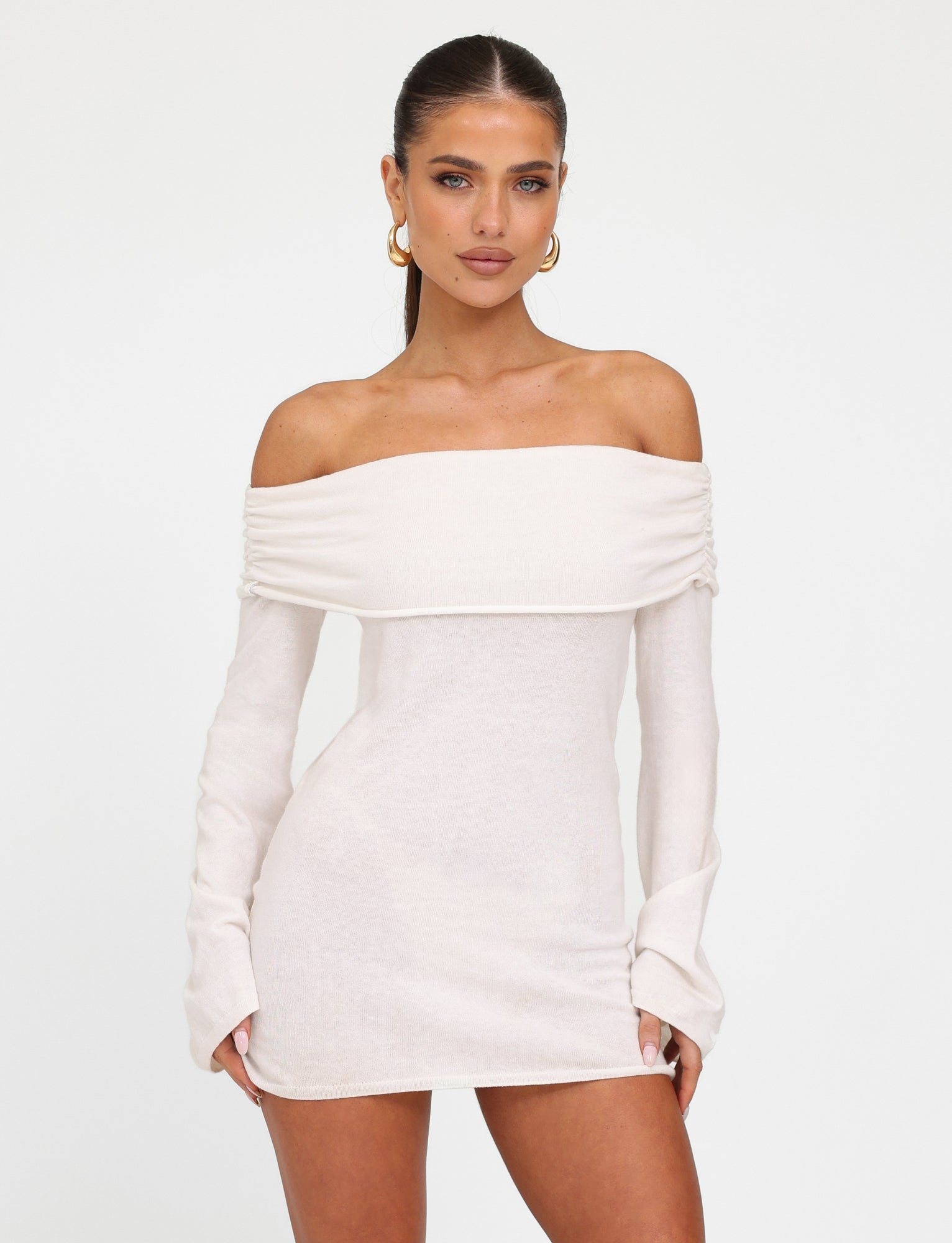 A woman with long, dark hair is wearing the DIEDRE JUMPER DRESS in WHITE and CREAM by TIGERMIST. She has gold hoop earrings and is standing against a plain white background, looking directly at the camera.