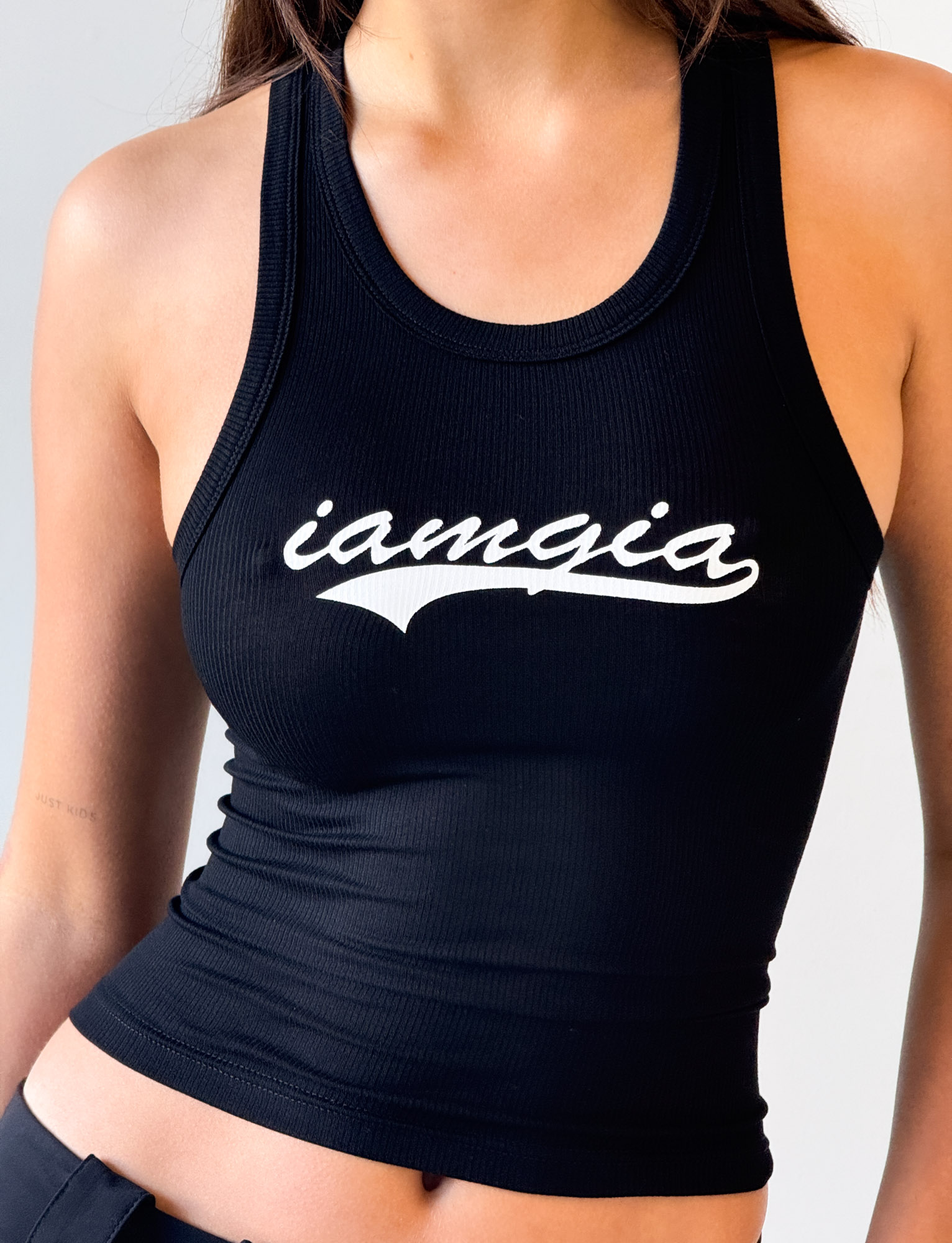 Someone wearing the I.AM.GIA PENELOPE TANK - GIA LOGO, a fitted black racer tank featuring "iamgia" in white cursive across the chest.