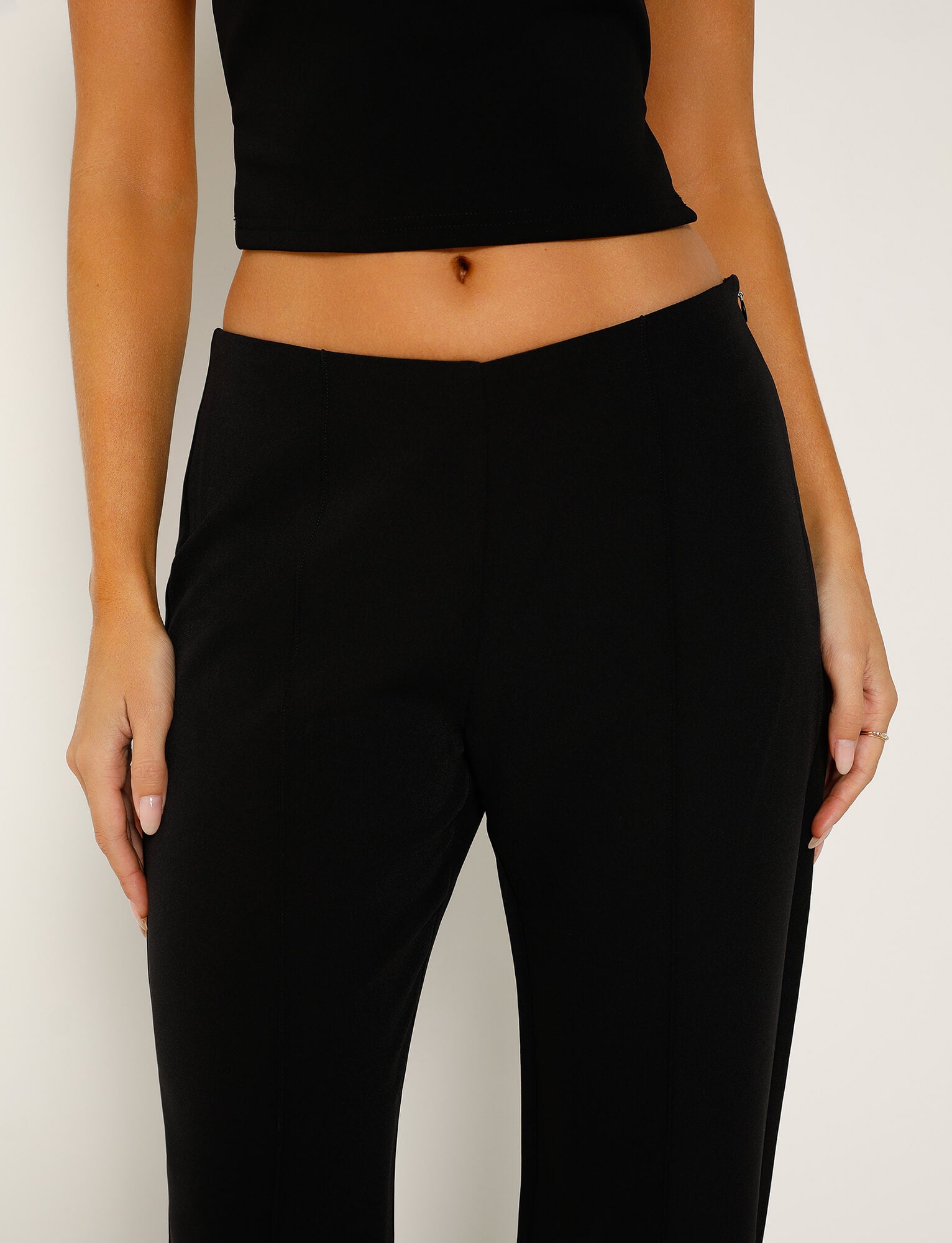 A person is shown from the chest down, wearing a black sleeveless crop top and high-waisted IAGO PANT - BLACK from TIGERMIST. The outfit highlights a small waist and offers a smooth, minimalistic look against a plain white background.