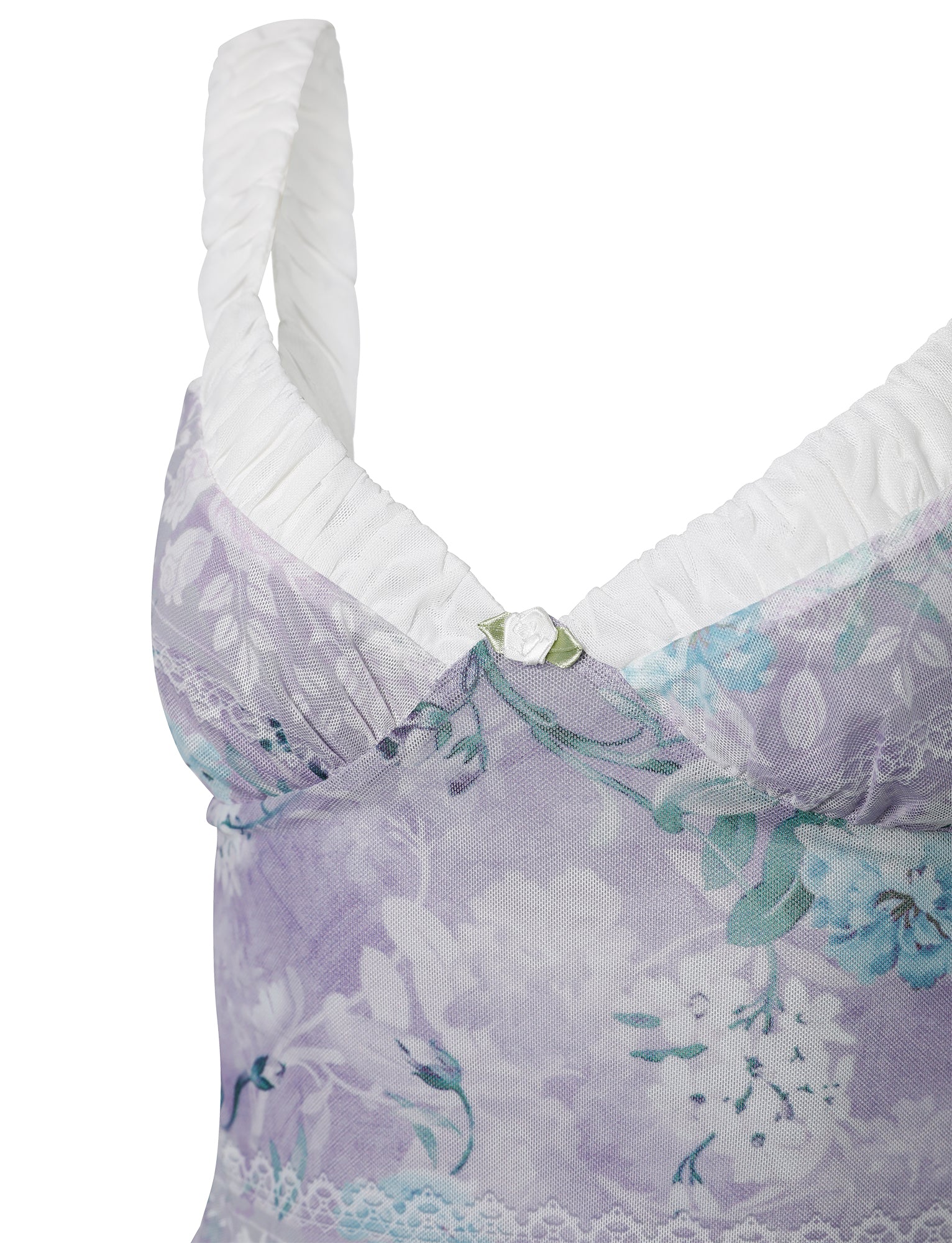 A close-up of the AMARAN TOP - PURPLE : FLORAL BOARDERS from TIGERMIST, showcasing its delicate floral pattern in shades of purple and green. The top edge is trimmed with white, textured fabric and features a small decorative metallic charm at the center.