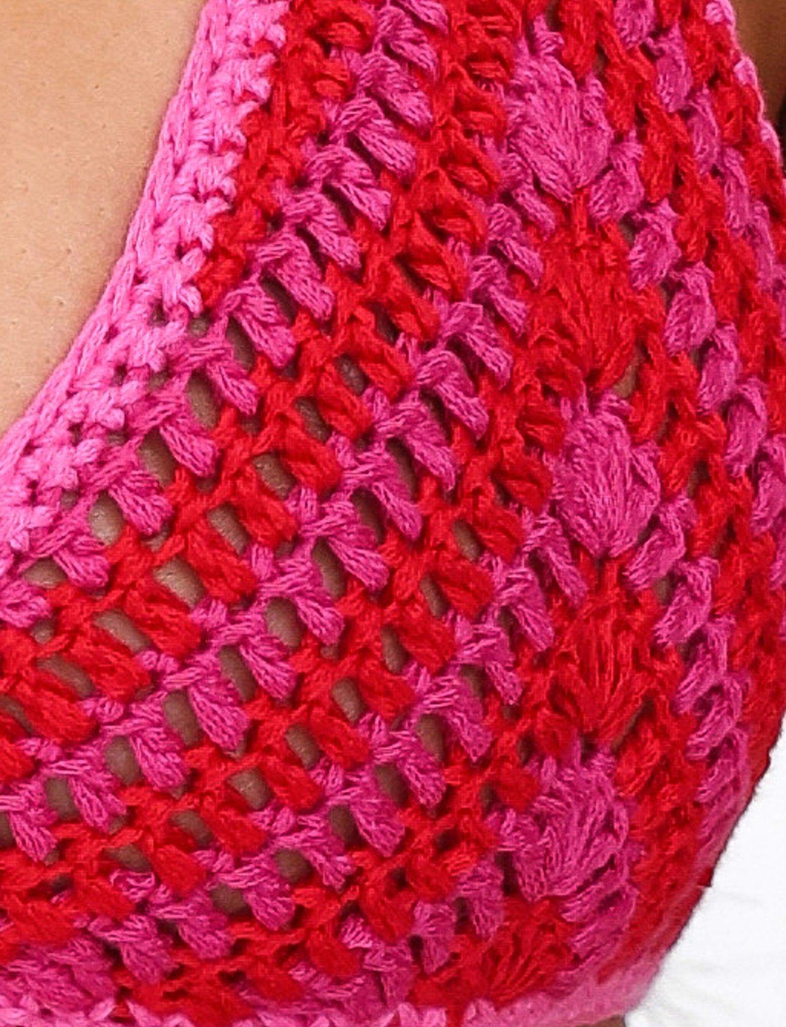 Close-up of the Cora Bikini Top - Pink : Stripe by TIGERMIST, featuring a vibrant pink and red striped pattern. This crocheted piece boasts an open, lattice-like texture and a fitted design, embodying the essence of wearable crochet fashion. The halter neck style allows part of the upper chest and edges to be visible.