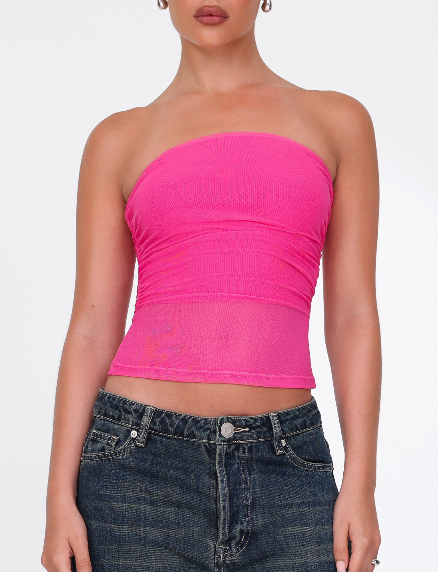 A woman wearing the TIGERMIST HARRIETT TUBE TOP in pink and high-waisted dark blue jeans stands against a plain white background.
