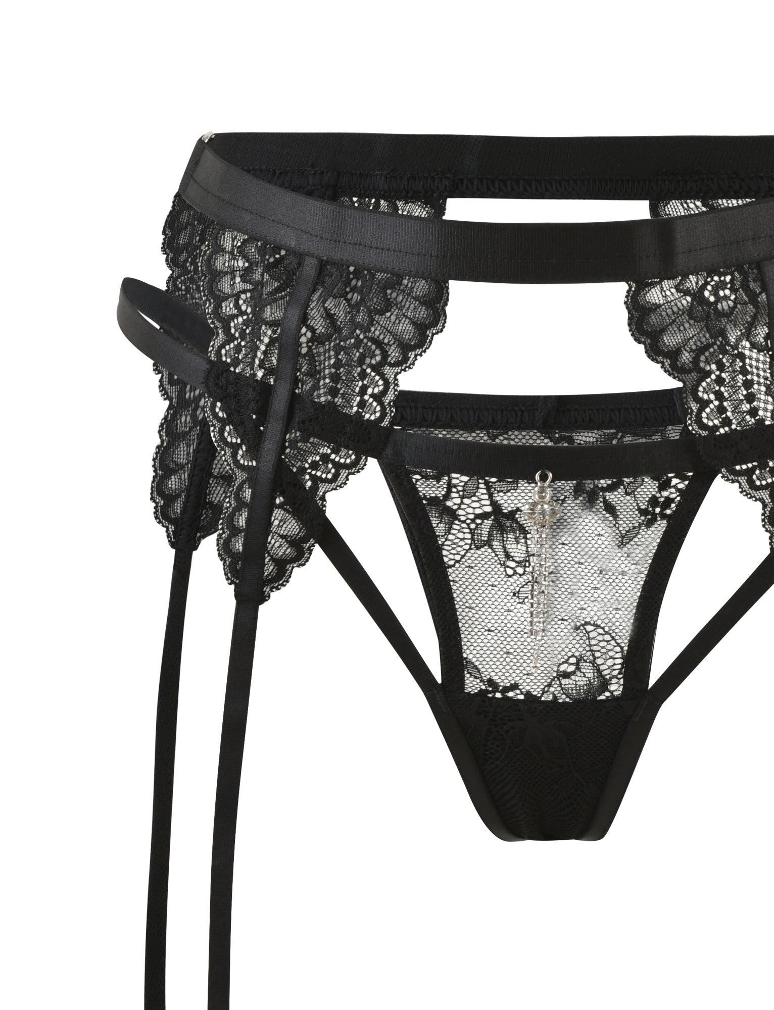 Close-up of the JORDAN SET - BLACK from TIGERMIST: a black lace garter belt with floral patterns, adjustable straps, and a silver charm. Part of an elegant and delicate lace intimate set with sheer mesh paneling for added detail.