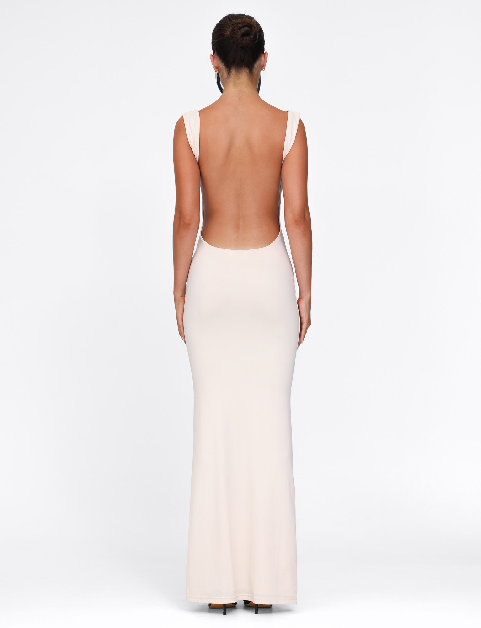 A woman with her hair in an updo poses against a white background, wearing the TIGERMIST MORANA DRESS - YELLOW : BUTTER—a long, sleeveless, backless bodycon dress. She is facing away from the camera.