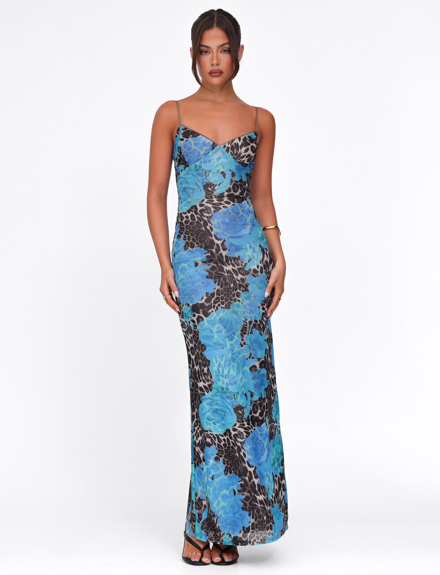 A woman stands against a white background wearing the TIGERMIST JULIANNA DRESS - BLUE : LEOPARD, a sleeveless maxi dress with blue floral and leopard print, paired with black sandals.