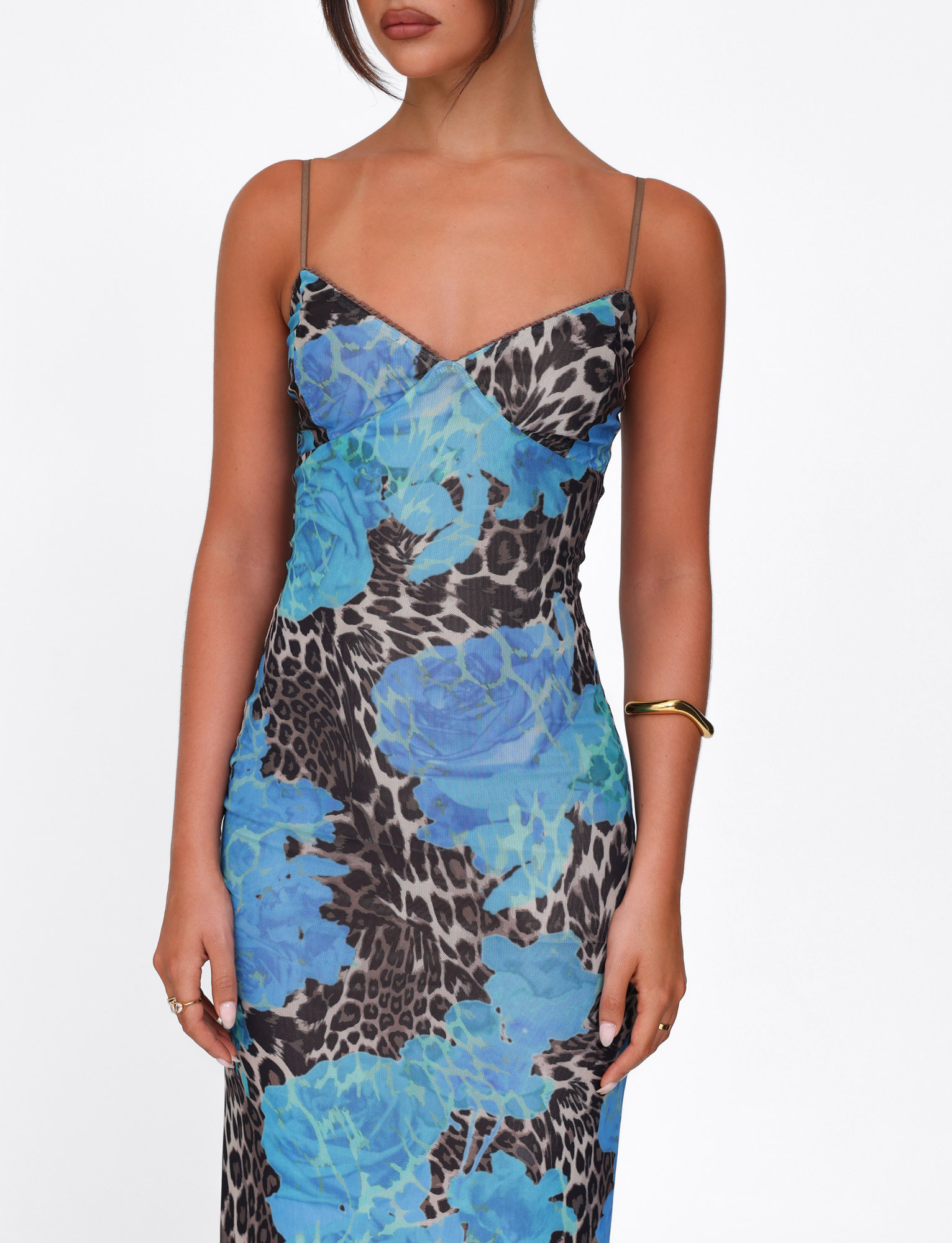 A woman in the TIGERMIST JULIANNA DRESS - BLUE : LEOPARD, a sleeveless spaghetti-strap maxi with blue floral and leopard print, stands against a plain white background, accessorized with gold jewelry. Her face is partially out of frame.