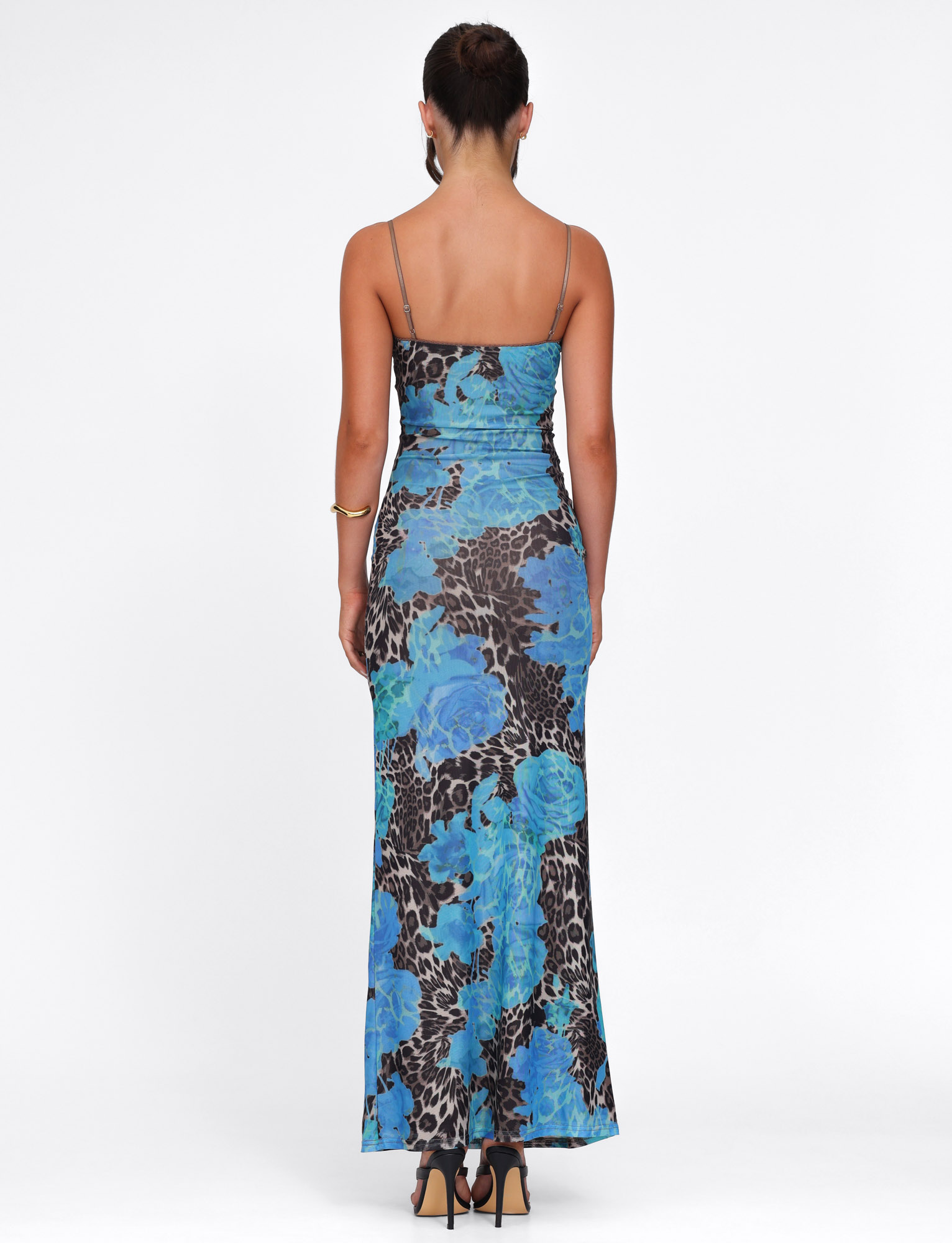 A woman stands with her back to the camera in the TIGERMIST JULIANNA DRESS - BLUE : LEOPARD, a long blue floral and leopard print dress with thin straps and a fitted silhouette, paired with black heels against a plain white background.