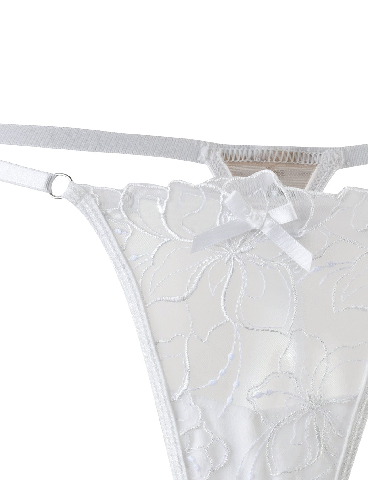 Close-up of the LAURA SET - WHITE by TIGERMIST, showcasing a white lace thong adorned with floral embroidery and a small bow decoration at the front. The semi-sheer fabric features delicate, intricate detailing along with visible elastic straps on the sides.