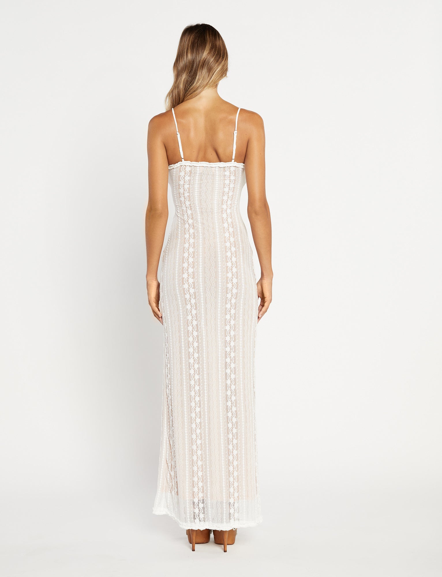 A woman stands facing away, showcasing the stunning SOPHA TWO PIECE MAXI DRESS - WHITE by TIGERMIST. Her long, wavy blonde hair cascades down her back as she poses against a plain white background.