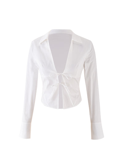 The ELVA SHIRT - WHITE from TIGERMIST is a stylish long-sleeve crop top featuring a deep V-neckline and chic tie-front closure. With its collar and cuffs, it exudes a semi-formal vibe, while the lightweight and slightly sheer fabric enhances its elegant appeal.