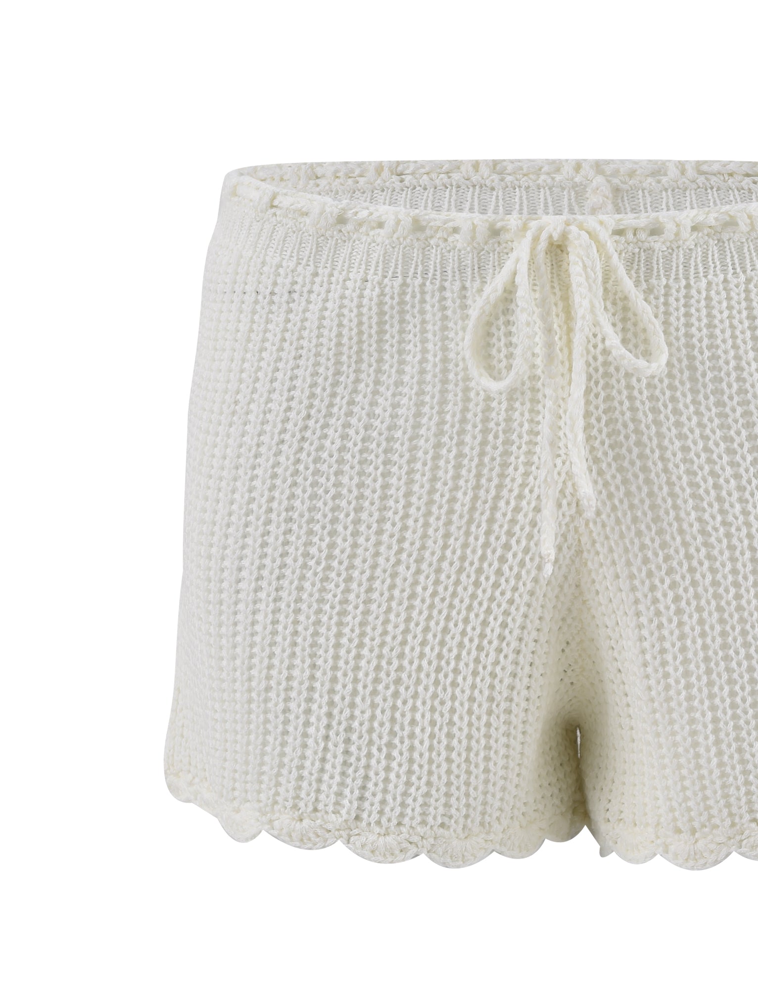 The RIKI SHORT in white, from the brand TIGERMIST, features a pair of soft knitted shorts with a scalloped hem and a drawstring waistband. The chunky, textured knit pattern provides a cozy and handmade look, making these shorts perfect for lounging or casual wear.