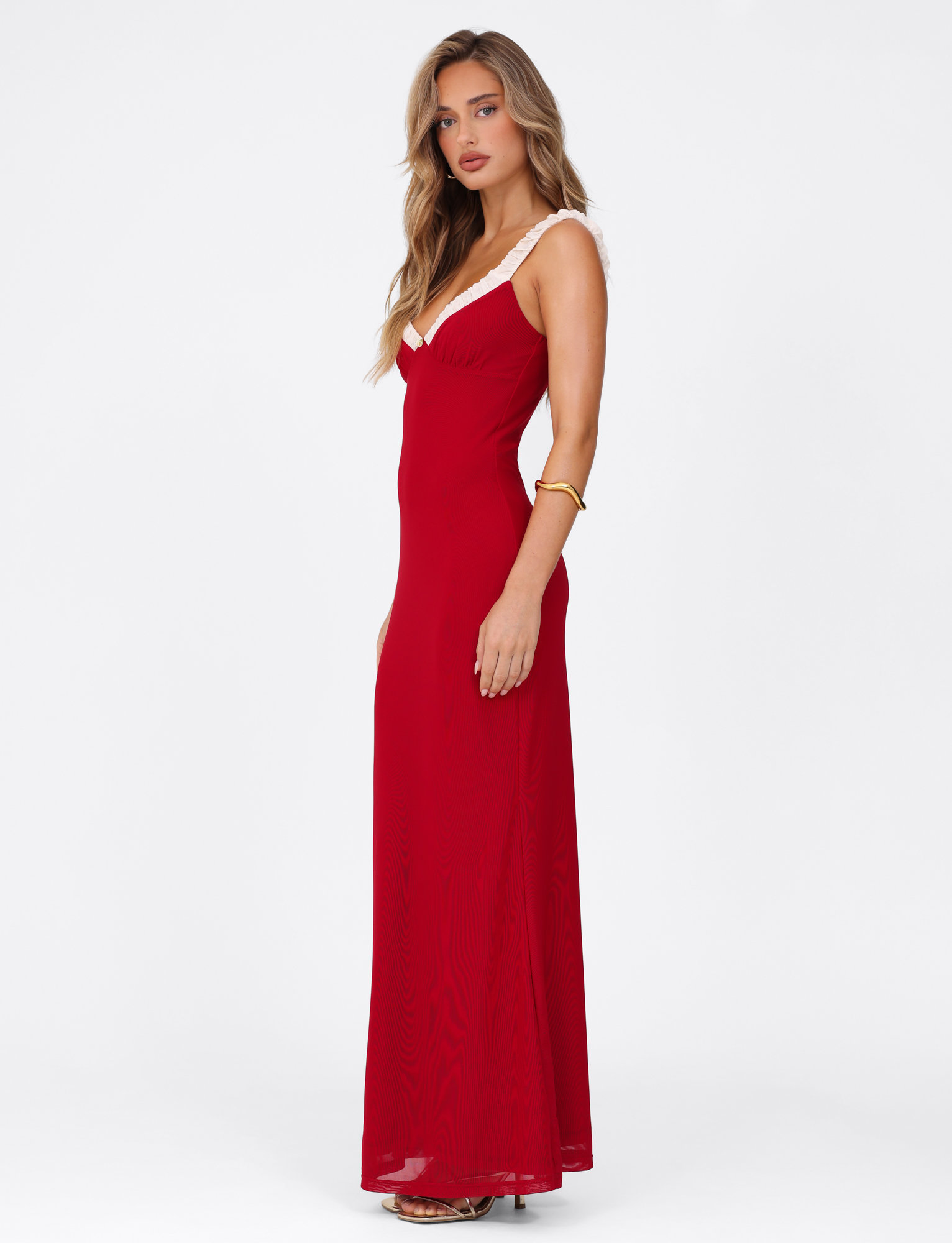 A woman with long, wavy blonde hair models the TIGERMIST AMARAN MAXI DRESS - RED : BURGUNDY, featuring white strap trim and an elegant bodycon fit. She wears gold bracelets and heeled sandals against a plain white background.