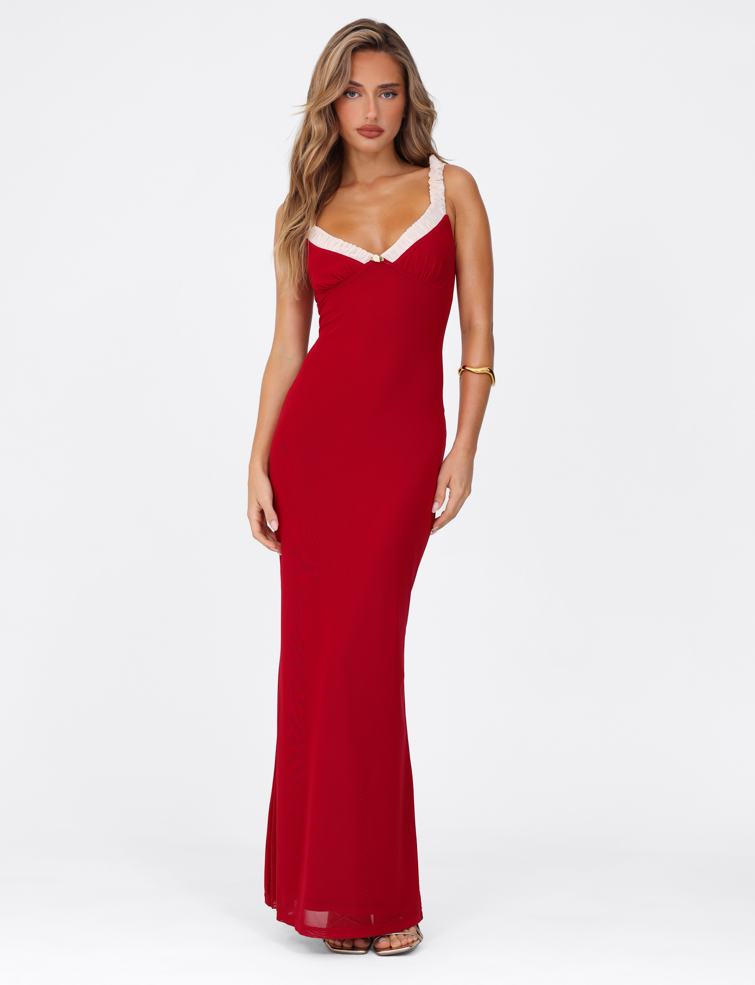 A woman stands against a white background in the TIGERMIST AMARAN MAXI DRESS - RED : BURGUNDY, featuring a bodycon silhouette and white lace-trimmed straps. She styles it with long wavy hair, a gold bracelet, and strappy heels.