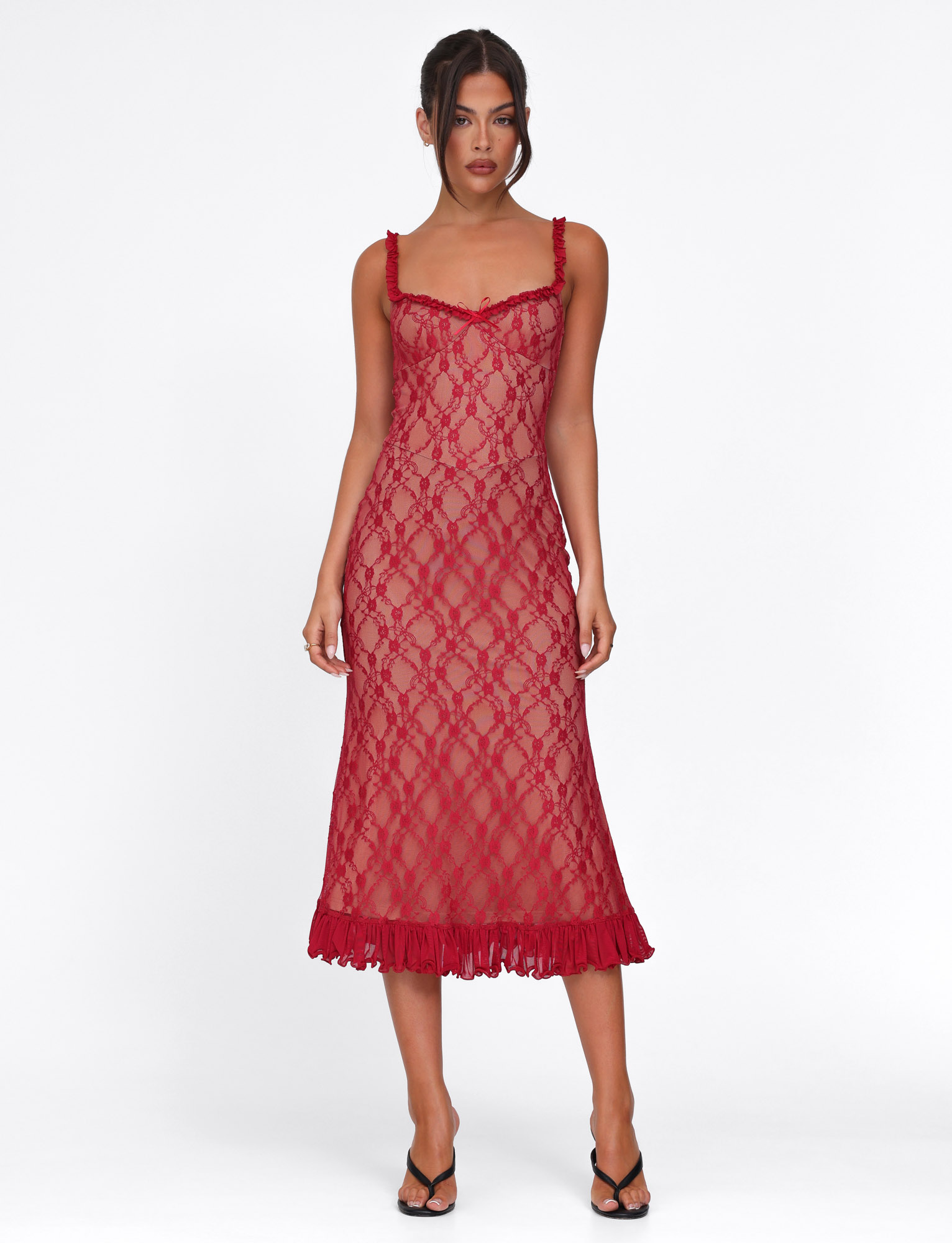 A woman stands against a white background wearing the TIGERMIST DEJA DRESS in Berry Red, a sleeveless sheer lace midi with a fitted silhouette and ruffled hem, paired with black strappy heels and her hair in a loose updo.