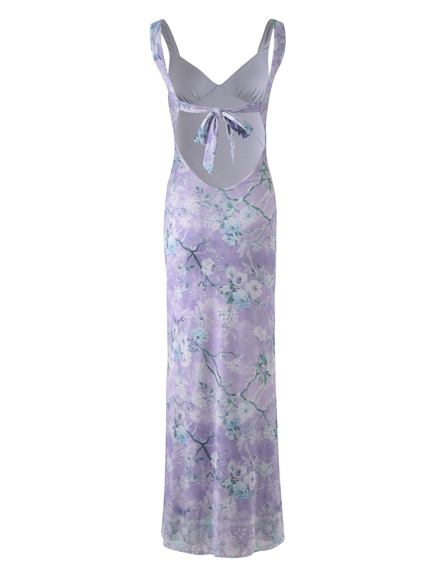 The KARMEN DRESS - PURPLE : FLORAL BOARDERS from TIGERMIST is a sleeveless, long dress in a light purple hue, adorned with floral patterns in shades of white and green. It features a keyhole cutout at the midriff tied with a matching bow, broad shoulder straps, and slightly sheen fabric that adds to its charm.