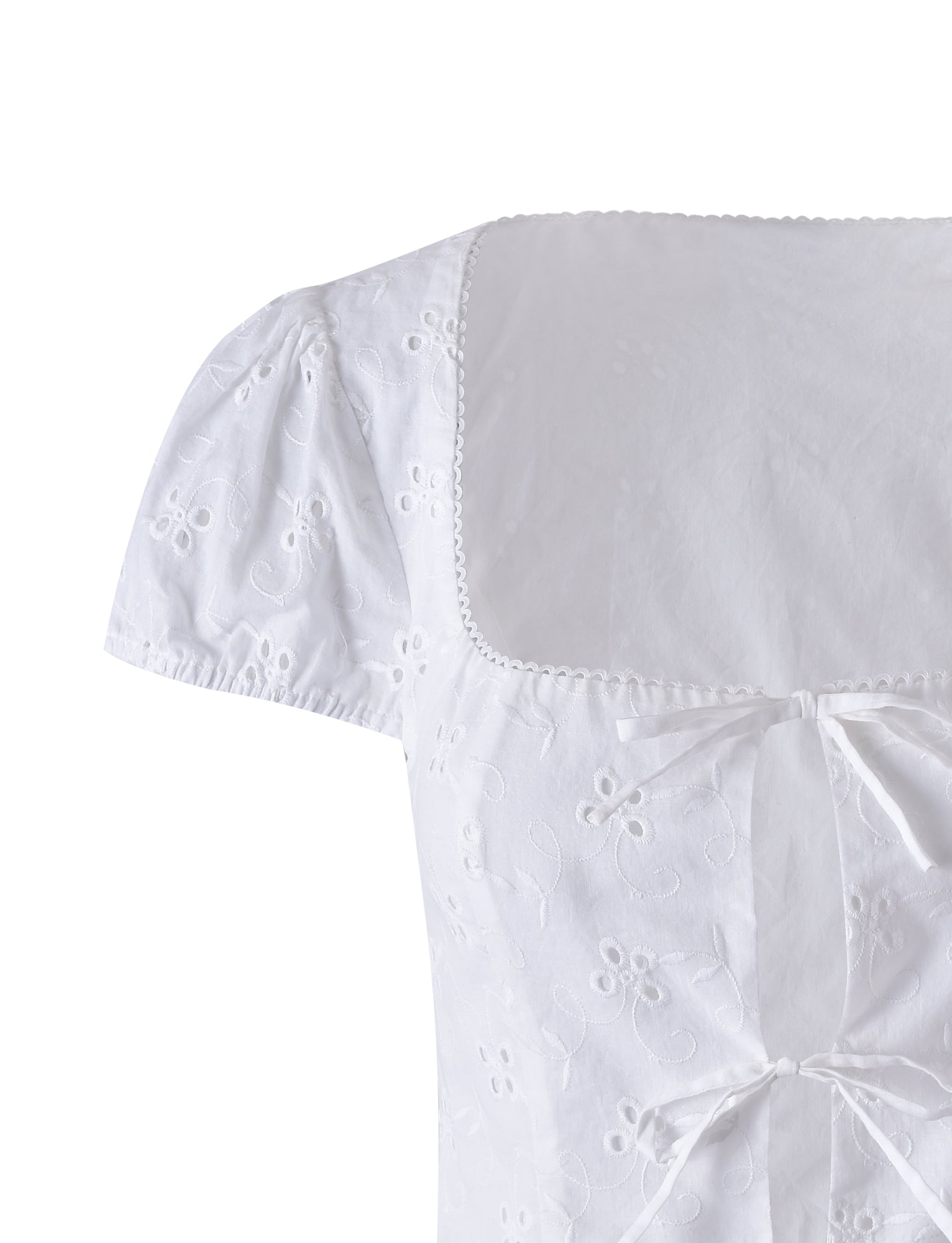 Close-up of the Kayleigh Top - White from TIGERMIST with a square neckline, puffed short sleeves, and delicate floral embroidery. The garment features two small bow ties at the front, adding to its elegant and feminine design. The fabric appears lightweight and breathable.