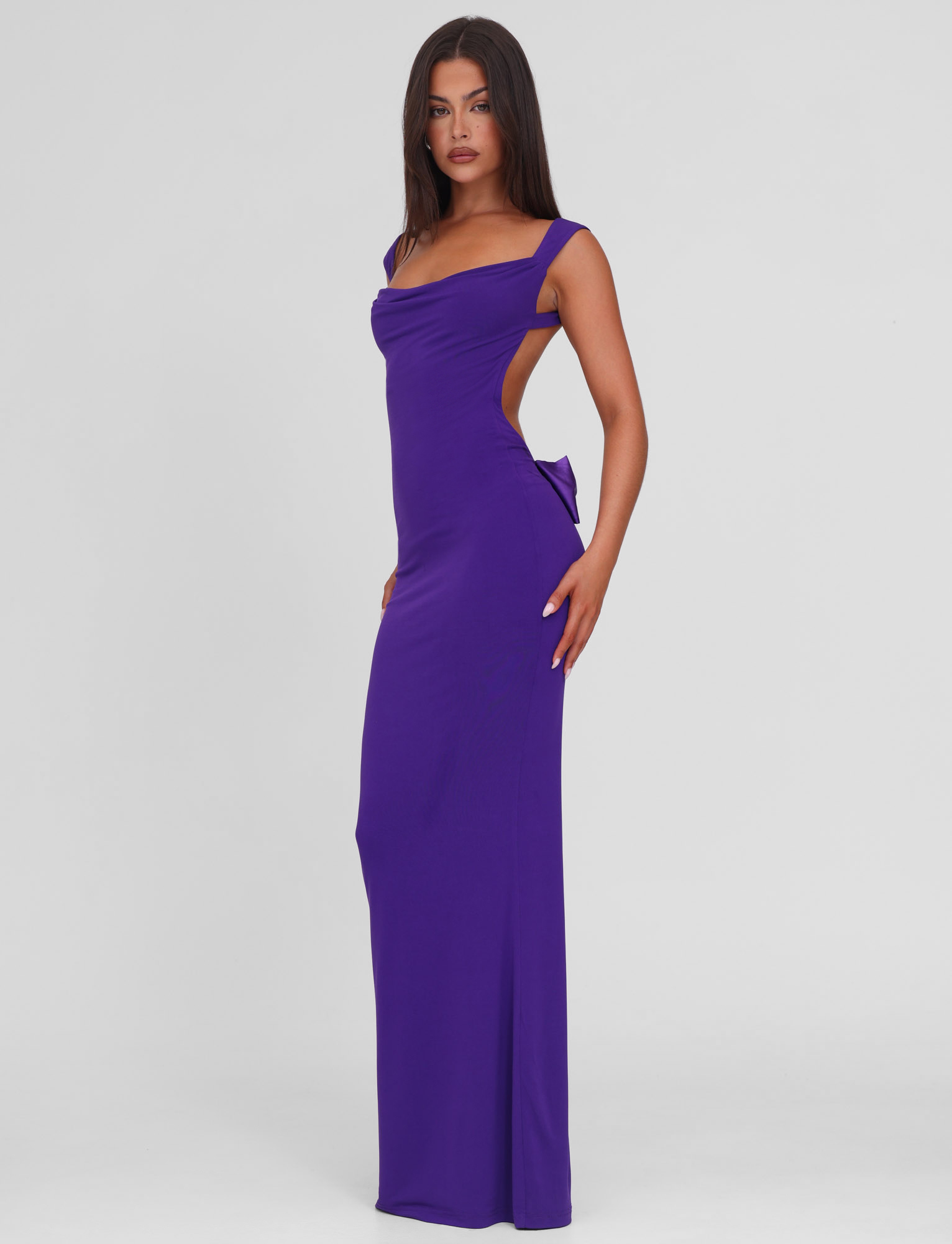 A woman models the TIGERMIST ZITA MAXI DRESS in purple, featuring a sleeveless design, open back, side detailing, and a bodycon fit that highlights her figure against a plain white background.