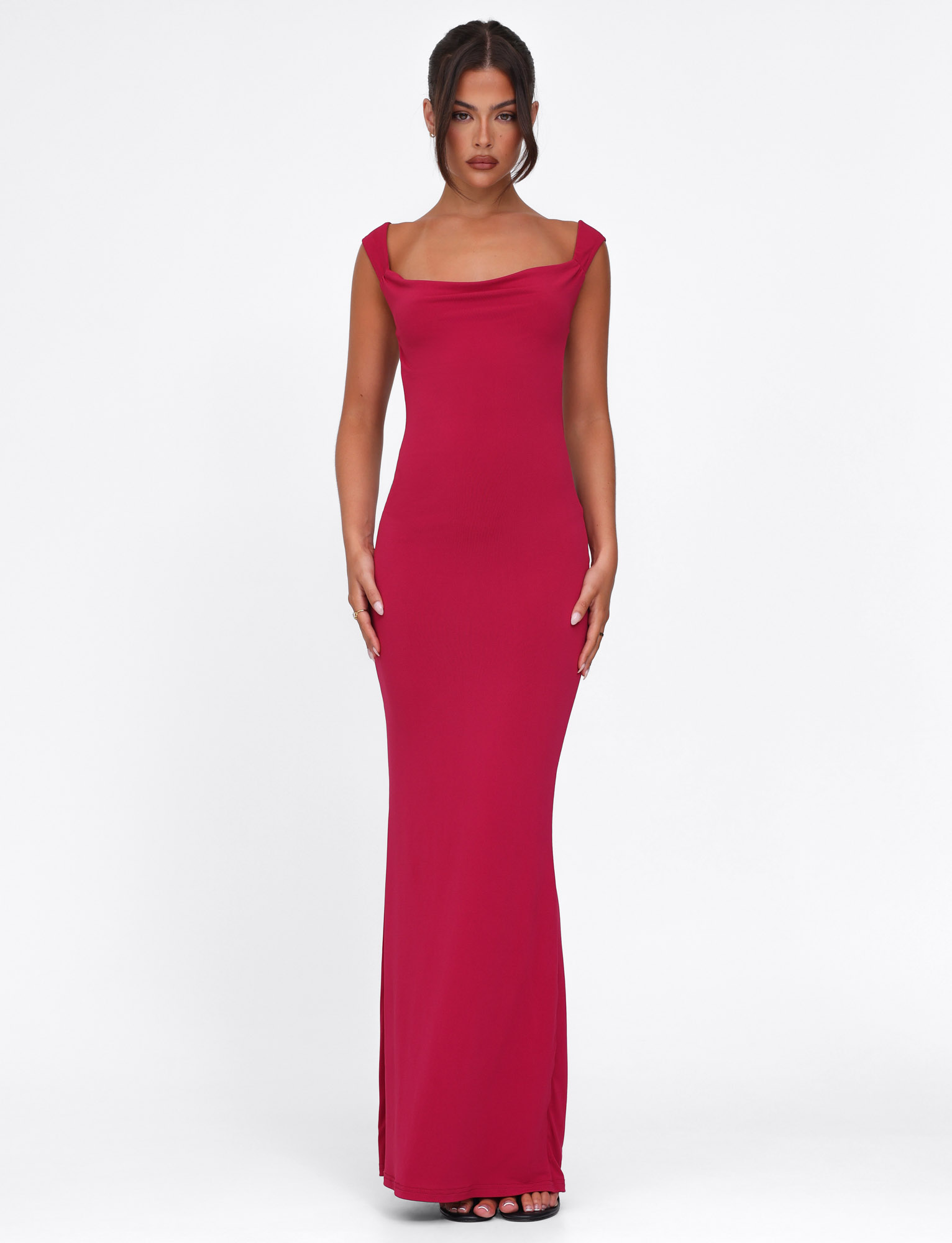 A woman stands facing forward in the TIGERMIST ZITA DRESS - RED : SALSA : DEEP RED, a fitted, floor-length maxi with a draped neckline. Her dark hair is styled in a sleek updo as she poses against a plain white background.