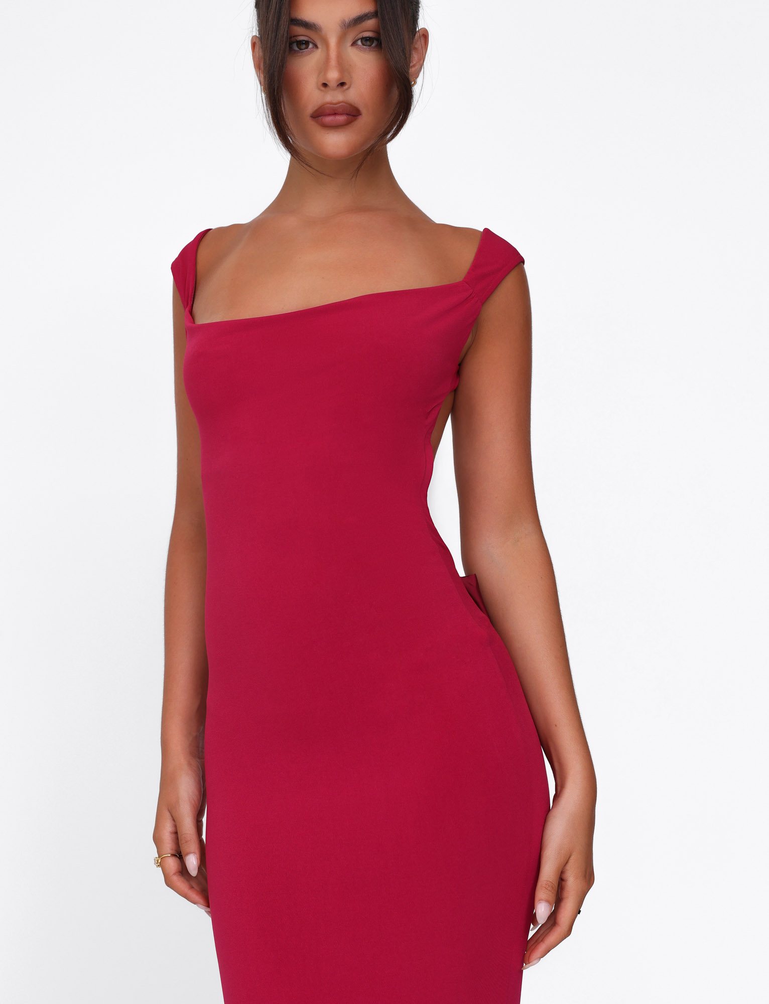 A woman wears the TIGERMIST ZITA DRESS - RED : SALSA : DEEP RED, a sleeveless, fitted deep red maxi with a square neckline and satin bow, standing against a plain white background.