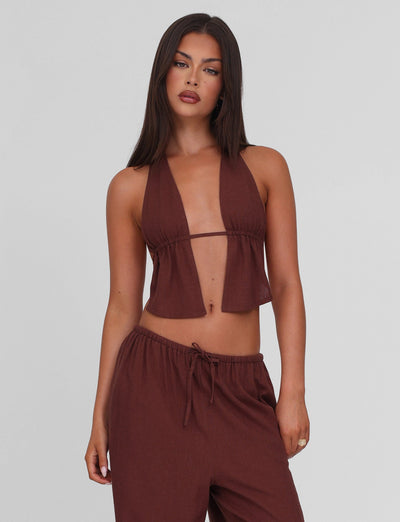 A woman with long dark hair models the TIGERMIST LAINEY TOP - CHOCOLATE, a linen halter top with adjustable ties, paired with matching drawstring pants against a plain light gray background.