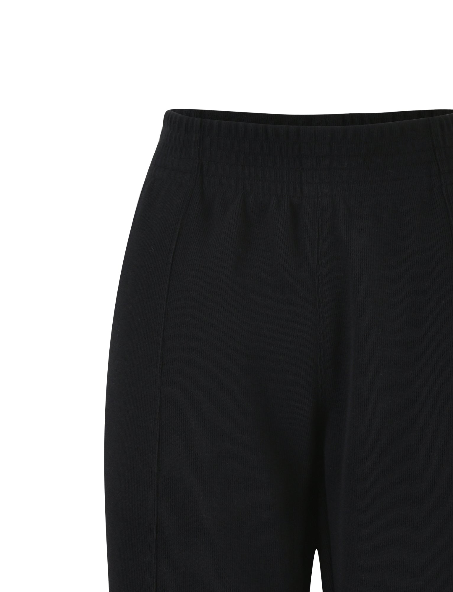 A close-up image of the VERDA PANT - BLACK by TIGERMIST. The pants feature an elastic waistband with visible stitching and a smooth, seamless front. The fabric appears to be soft and slightly stretchy. The image focuses on the upper portion of the pants, ending just above the knees.