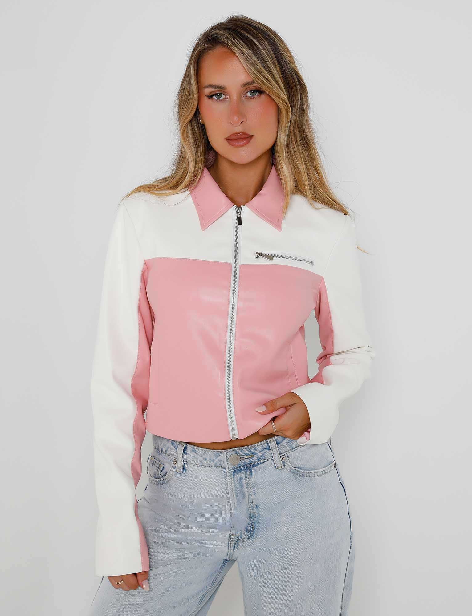 A person with long, wavy blonde hair wearing a TIGERMIST DELIA JACKET - PINK : PINK/WHITE and light-wash jeans poses against a plain white background. They are standing with one hand in their pocket and the other resting near their waist.