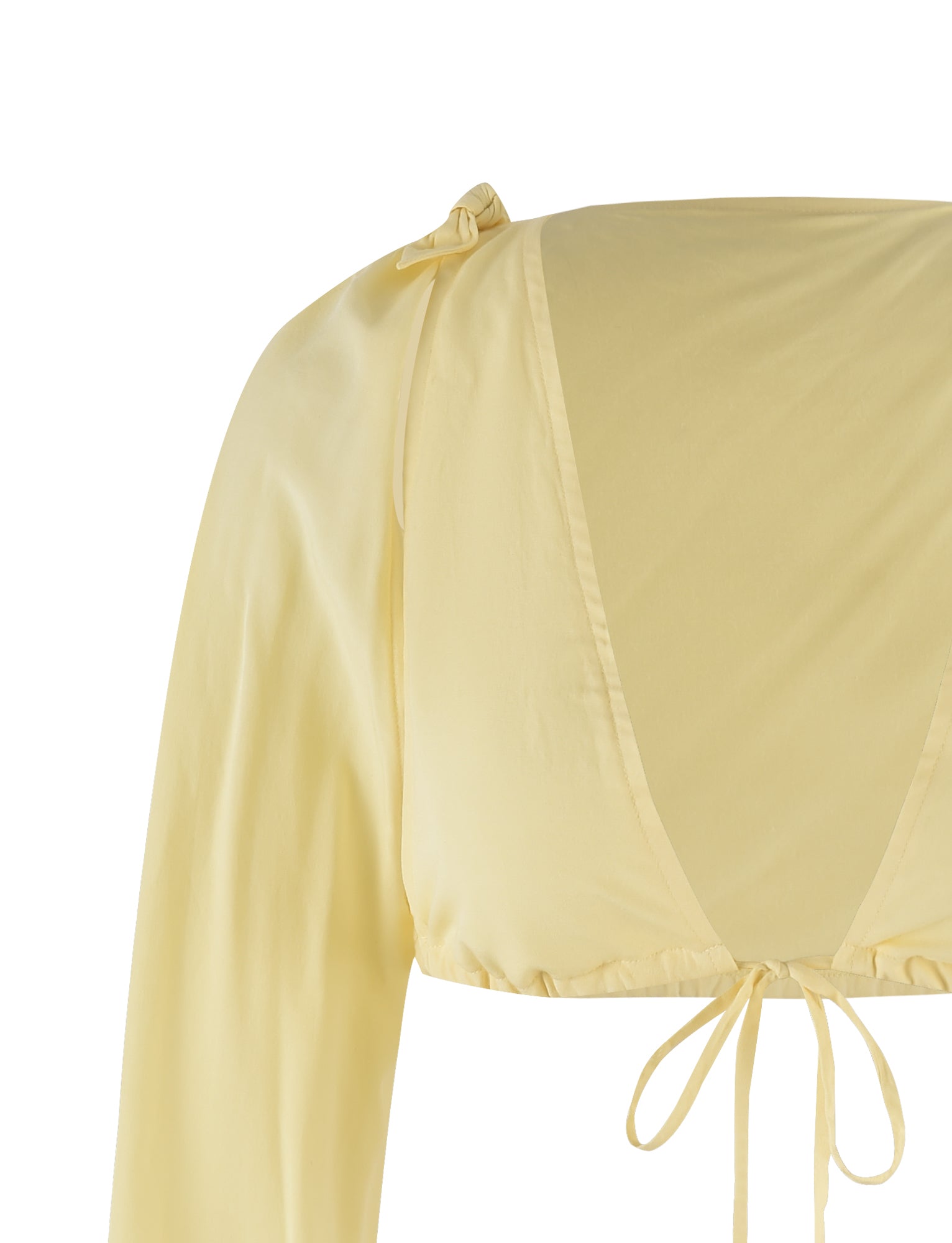 Close-up image of the PHILLIPA TOP - YELLOW : LEMON from TIGERMIST. This light yellow long-sleeve blouse features a deep V-neckline with a tying detail at the bottom and a subtle bow accent on one shoulder. The fabric appears soft and flowy, against a plain white background.