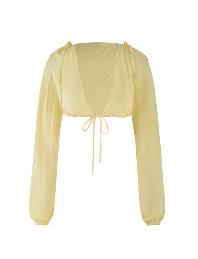 The PHILLIPA TOP - YELLOW : LEMON from TIGERMIST is a light yellow, long-sleeved crop top that features a deep V-neckline, tie-front closure, and slightly puffed sleeves with elasticized cuffs. The soft and lightweight fabric creates a casual yet stylish look.
