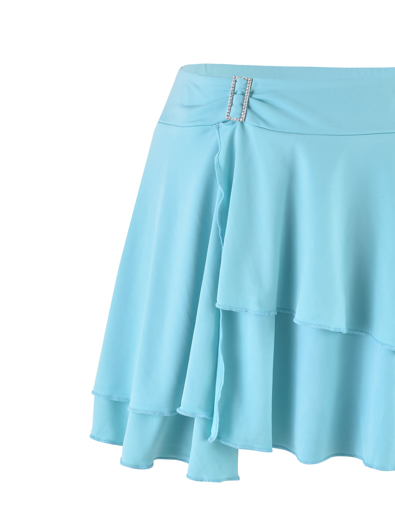 Introducing the VERANIQUE SKIRT - BLUE by TIGERMIST: This light blue, flowy skirt features tiered layers and a fitted waistband embellished with a small, rectangular rhinestone on one side. The lightweight fabric adds a slightly ruffled effect at the edges.