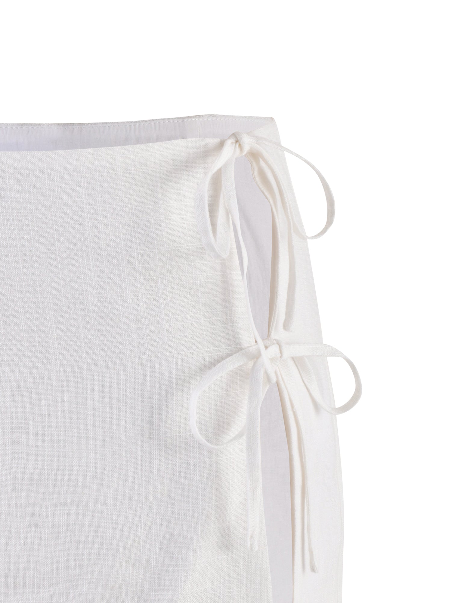 A close-up of the TIGERMIST NICOLA SKIRT - WHITE showcases two tied bows on the right side. The skirt's fabric features a textured pattern with subtle vertical and horizontal lines, creating a checkered appearance. The edges are neatly hemmed.