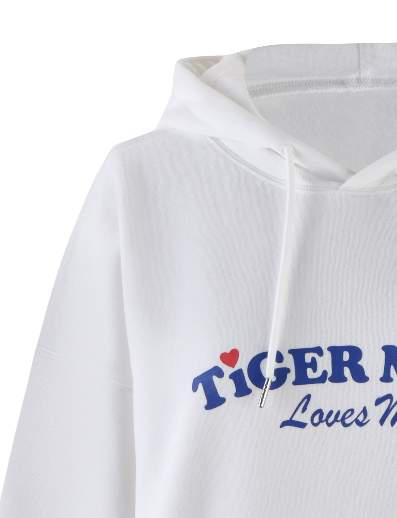 Close-up of the LUMEN HOODIE - WHITE by TIGERMIST, a white loungewear hoodie with a hood and drawstrings. This oversized silhouette features blue text that reads "TIGER" with a small red heart for the dot above the "I," along with additional text below in smaller blue font reading "Loves Never." A cozy kangaroo pocket completes the look.