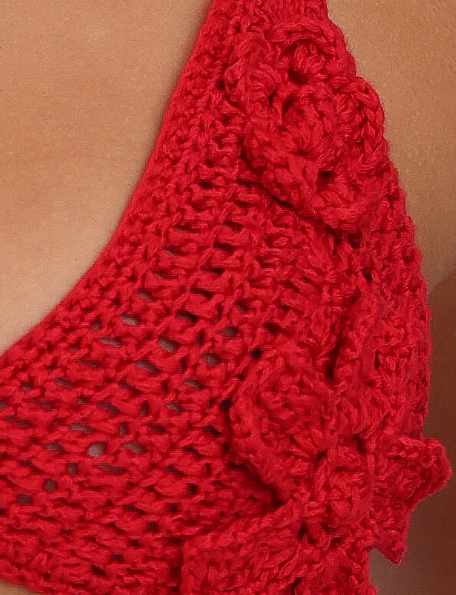 Close-up of the TIGERMIST MELIORA BIKINI TOP - RED : BERRY RED, featuring intricate floral patterns. The texture and detail of the crochet work are prominently displayed, showcasing delicate craftsmanship. This semi-sheer material suggests an elegant bikini top set against a skin-toned background.