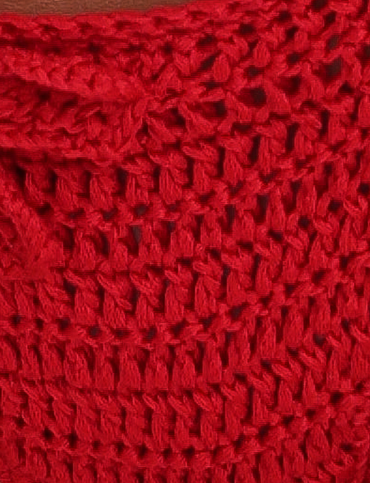 Close-up of the MELIORA BIKINI BOTTOM - RED : BERRY RED by TIGERMIST, showcasing a textured crochet pattern made up of interlocking loops. The yarn looks thick with a slightly open weave, creating a rich and tactile surface reminiscent of fashionable crochet swimwear or stylish red bikini bottoms.