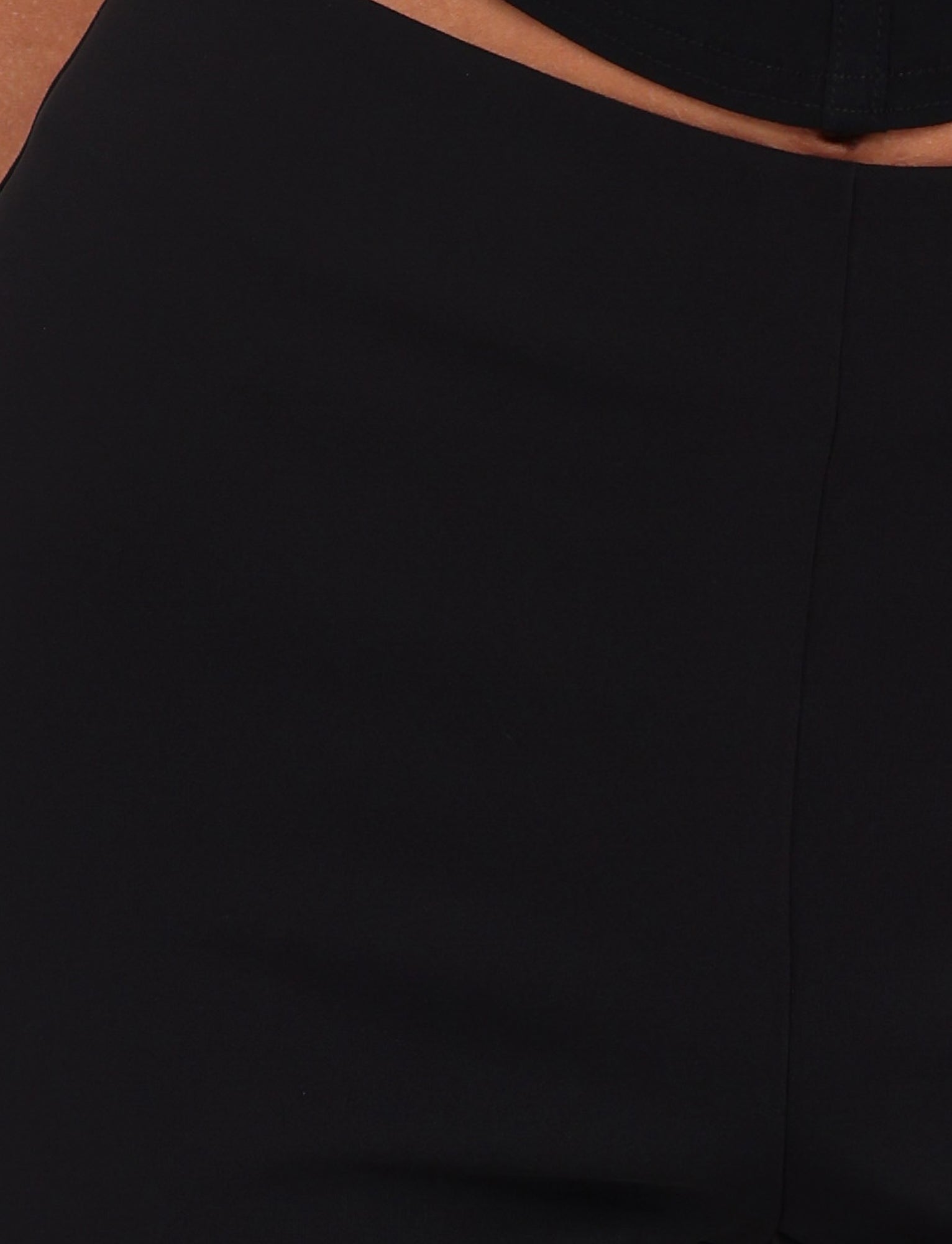 Close-up view of a person wearing the DAMIRA PANT in black from TIGERMIST. The focus is on the midsection and upper thigh area of the pants, showcasing their impeccable texture and fit.