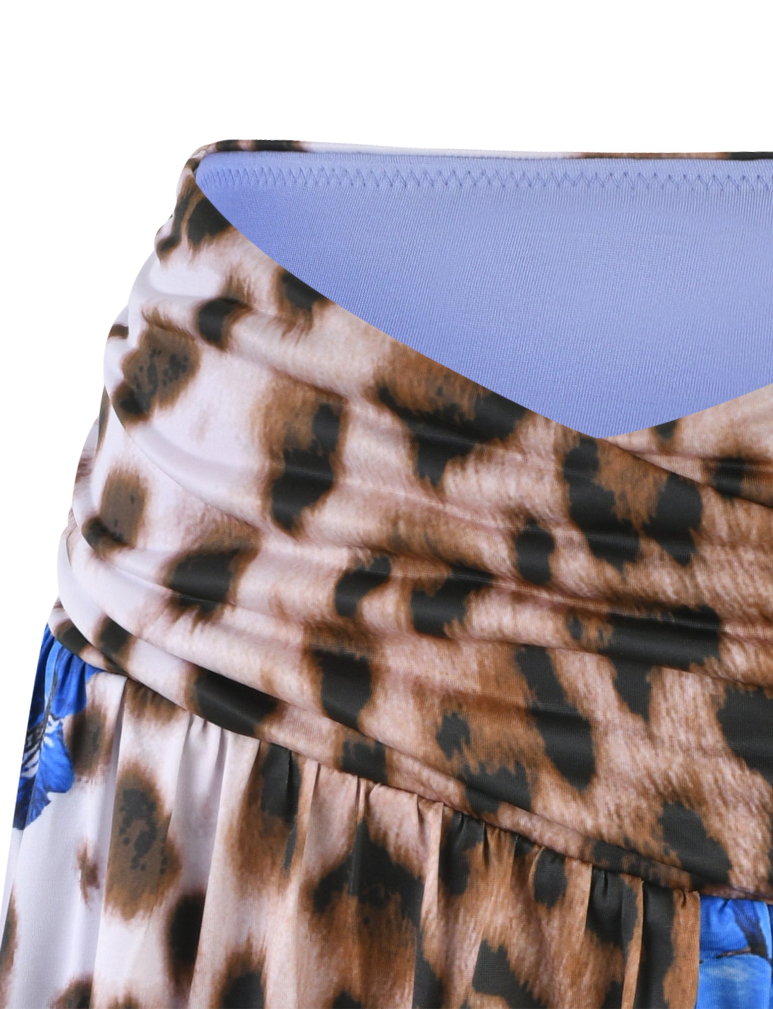 A close-up of the BRIXLEY SKORT from TIGERMIST showcasing a Leopard-print fabric with light brown and black spots. The skort features a blue lining visible at the inner edge and is slightly gathered, creating a draped effect. Small blue floral accents adorn the bottom edge of the image.