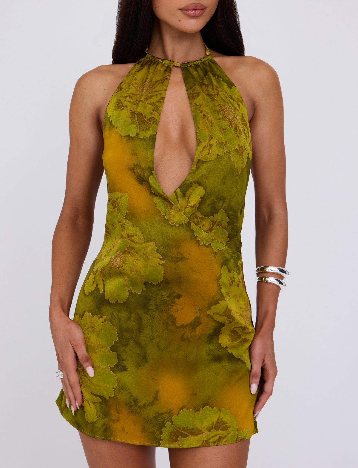 Model shown from shoulders to mid-thigh wearing the TIGERMIST MONROE DRESS - GREEN : WATER COLOUR FLORAL, a sleeveless dress with a halter neckline and front keyhole cutout, styled with silver bracelets and rings.