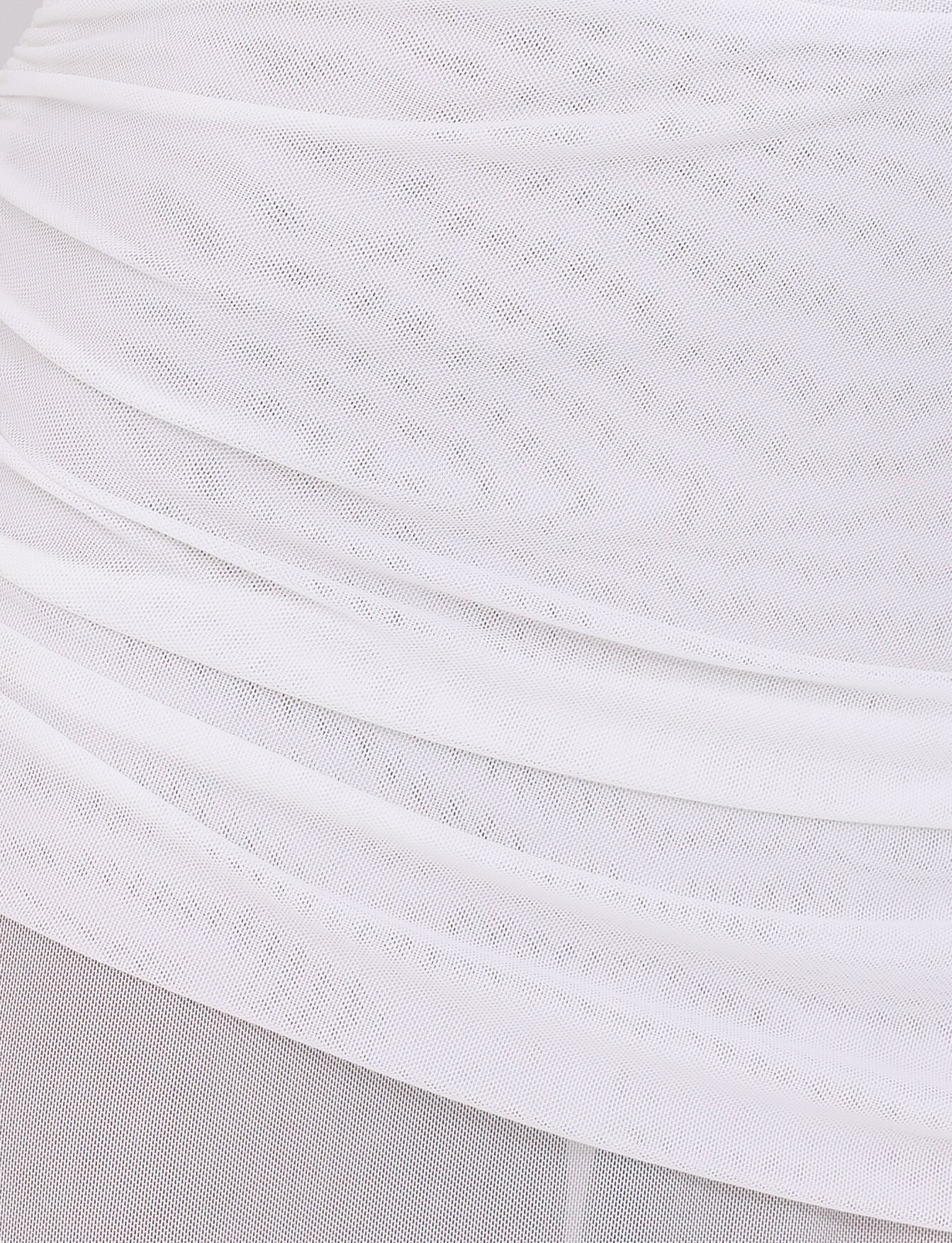 A close-up view of the ESHA MAXI DRESS - WHITE by TIGERMIST reveals a transparent fabric with layered, ruched detailing that echoes its bodycon silhouette. The textured appearance gently enhances the maxi length as light softly diffuses through the delicate material.