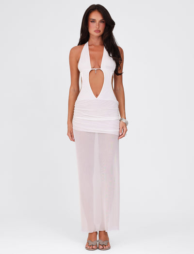 A woman models the ESHA MAXI DRESS in white from TIGERMIST, showcasing its halter-neck style and deep keyhole cutout against a plain backdrop. The semi-sheer gown elegantly cascades to the floor in a maxi length. She completes her look with sandals and long, dark hair.