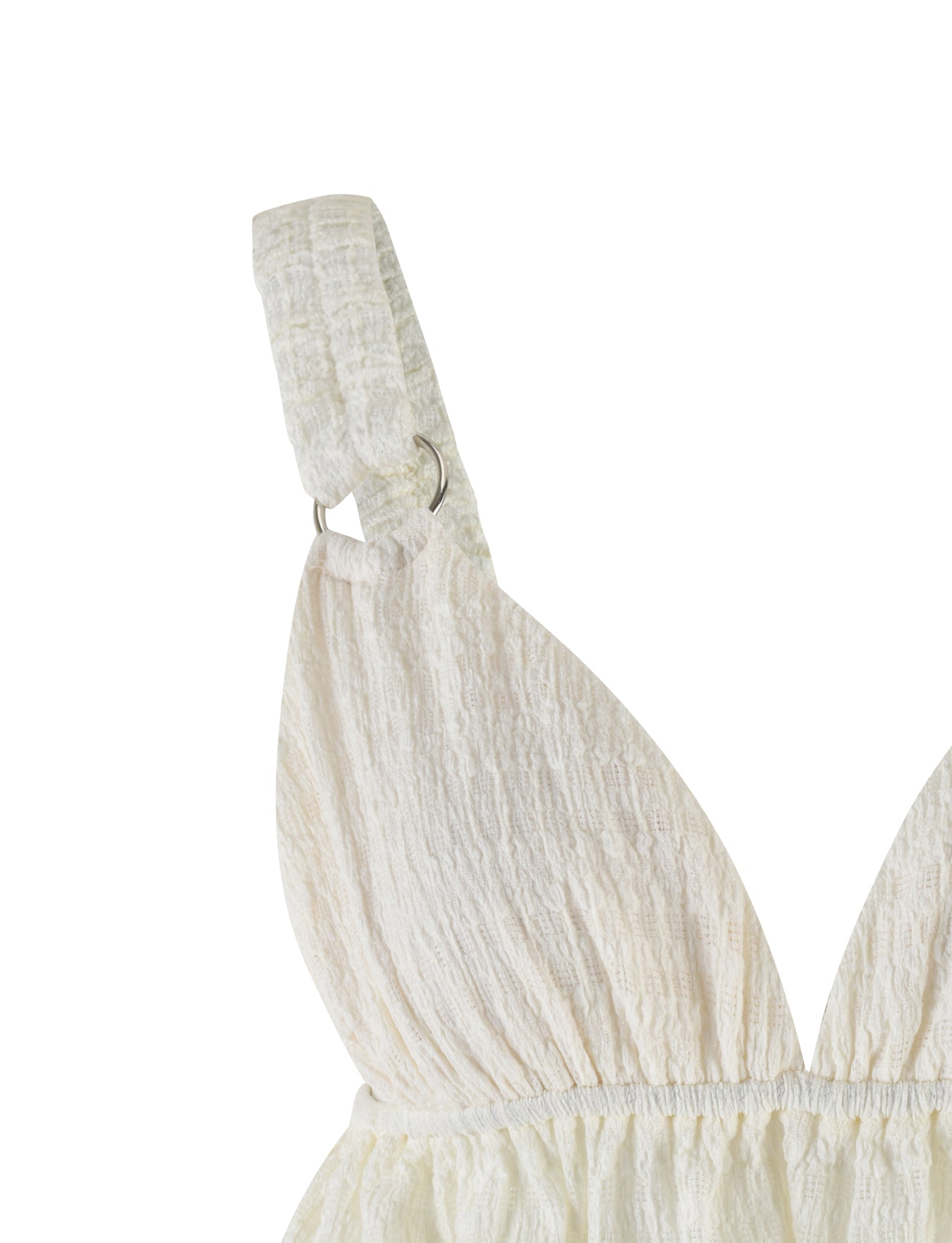 Close-up image of the ALDRIDGE TOP - WHITE by TIGERMIST, showcasing a light cream-colored textured jersey garment with a ruched design and wide shoulder straps accented by metal rings. The crop length fabric features a subtle, crinkled appearance, giving it a casual and modern look. The background is plain white.