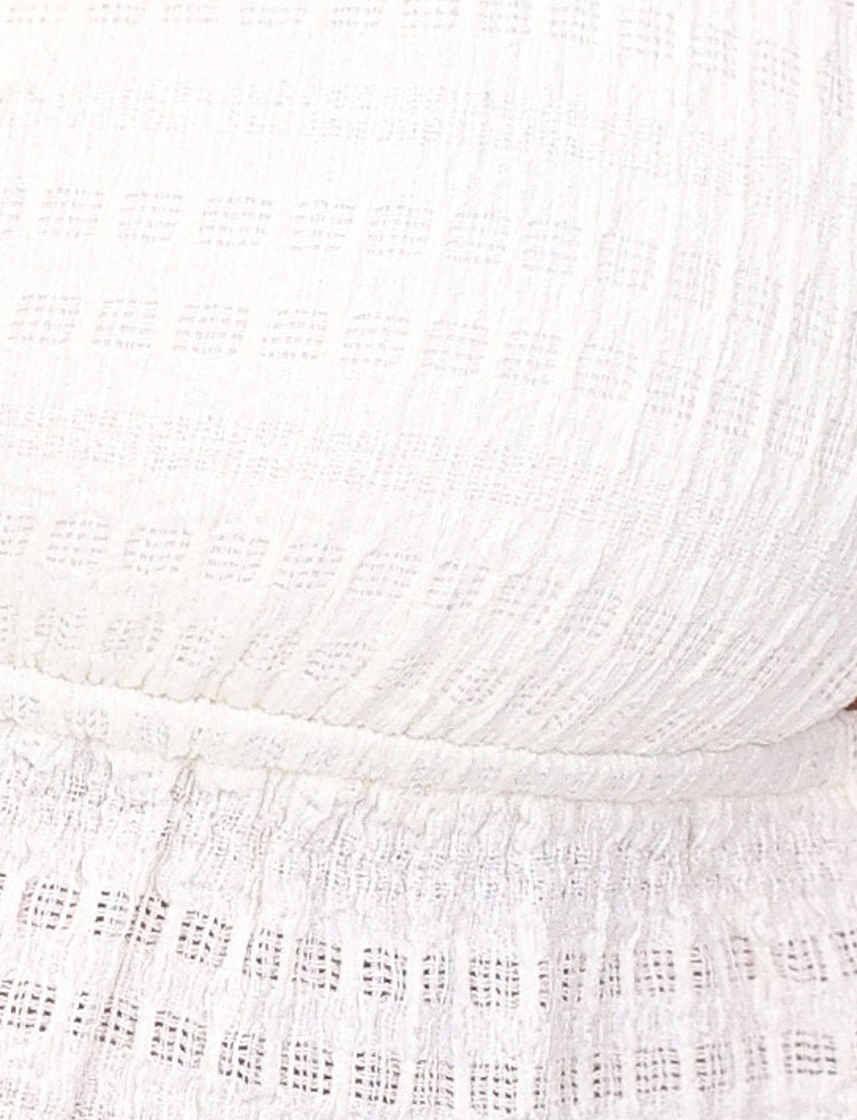 Close-up image of the ALDRIDGE TOP - WHITE by TIGERMIST, showcasing its white textured jersey fabric with a grid-like pattern. The material features a snug fit with gathered and slightly ruffled details near the bottom edge, resembling a crop-length camisole top.