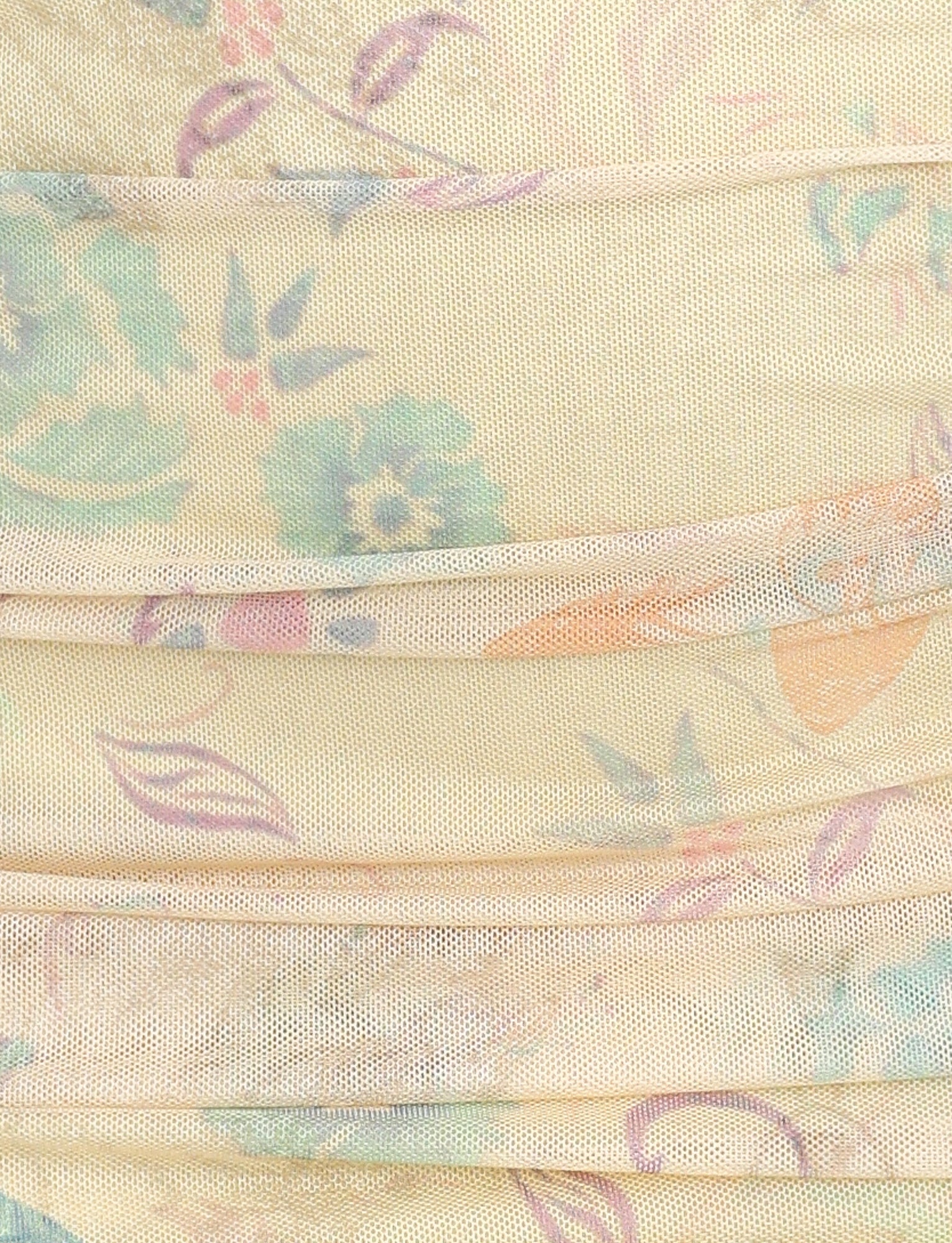 A close-up of the textured fabric surface of the KERR DRESS - YELLOW: DELICATE FLORAL by TIGERMIST showcases its pastel floral print in shades of blue, pink, and purple. The fabric is lightly pleated or gathered, creating a series of parallel folds on this mesh fabrication dress. The background color is a soft beige or light cream.
