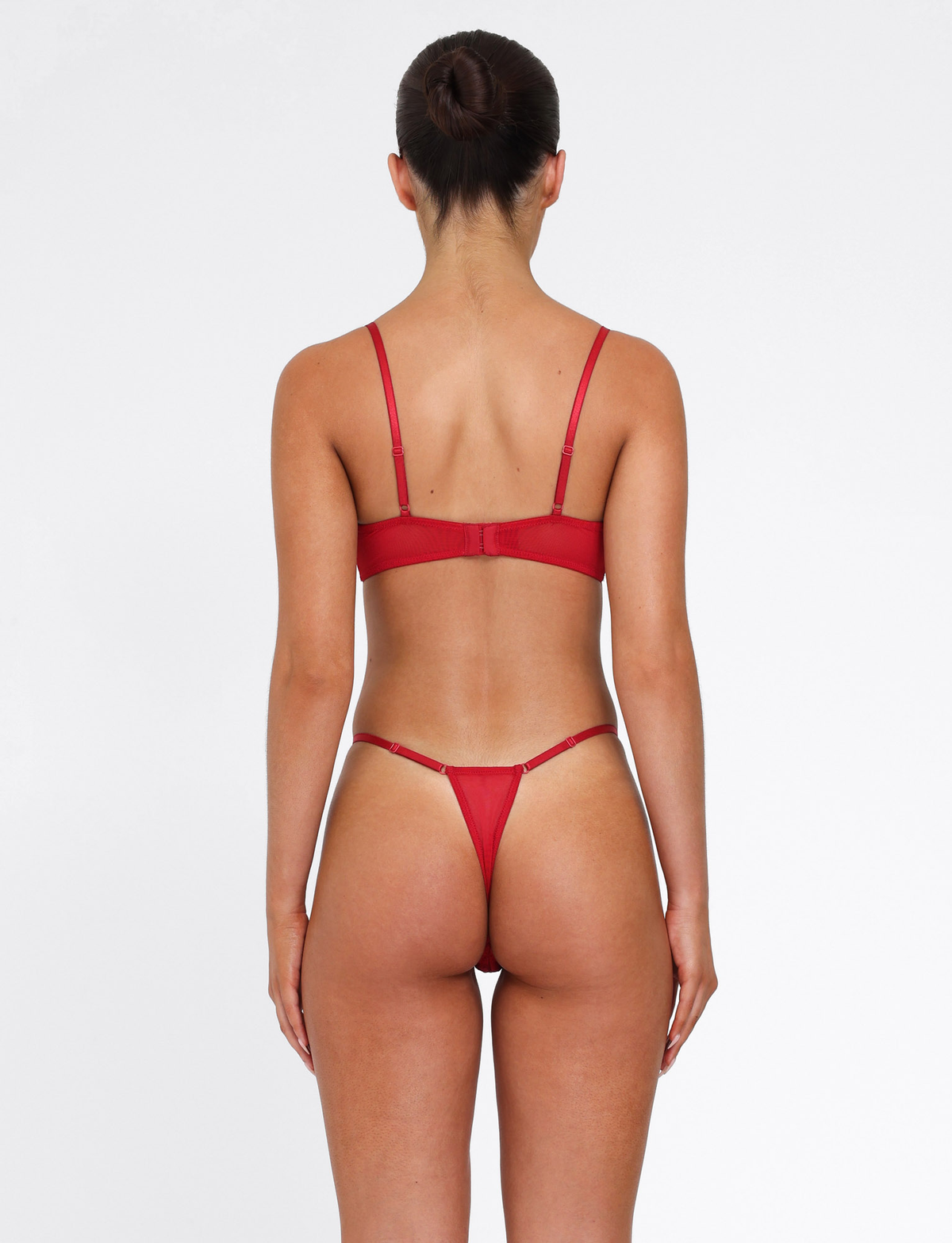 A woman with dark hair in a bun stands with her back to the camera, modeling the TIGERMIST TALIYAH SET - RED, featuring an embroidered mesh bra and g-string, against a plain white background.