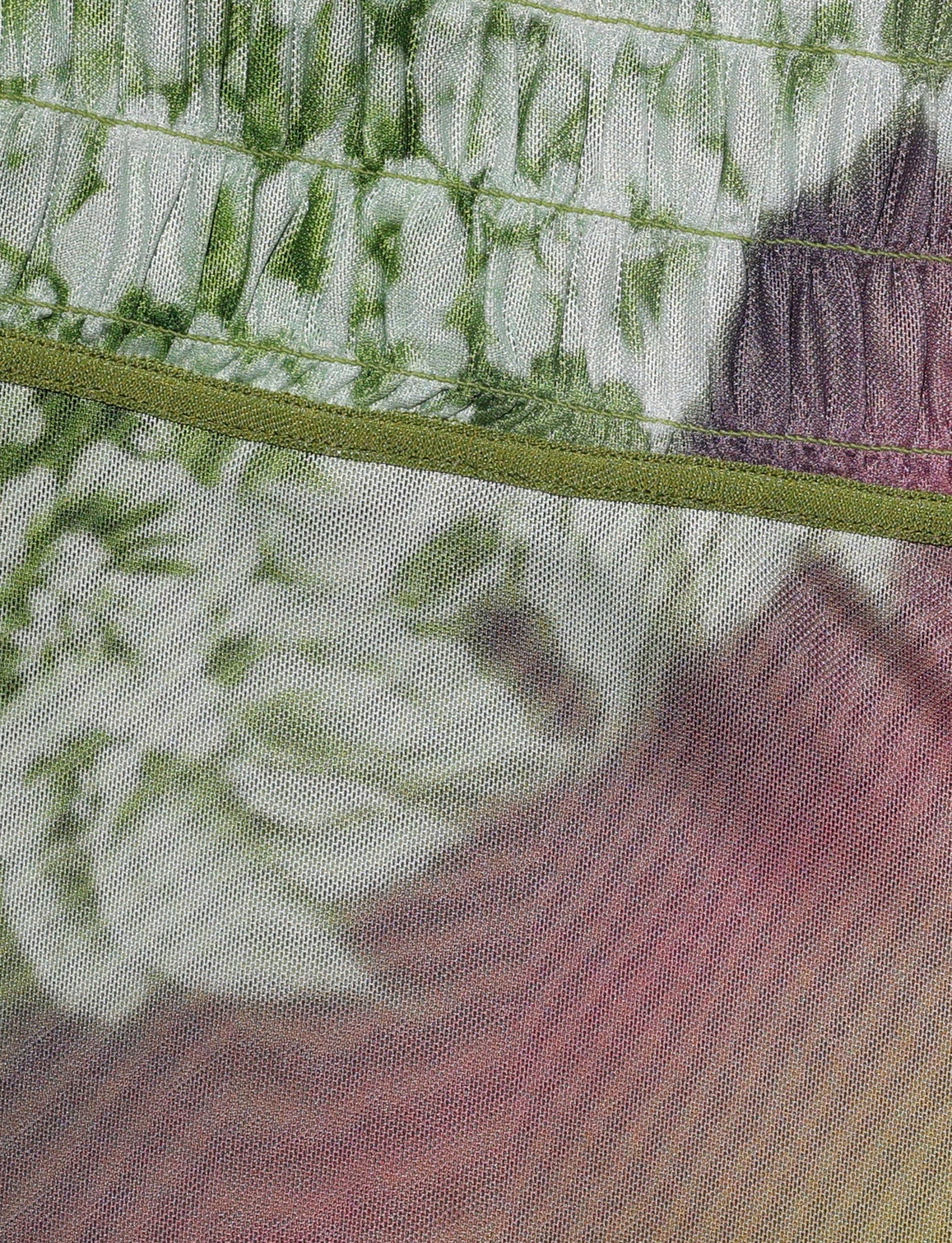 Close-up of the WAVERLY SKIRT from TIGERMIST, showcasing its ruched texture and vibrant tie-dye pattern in shades of green, white, and pink/purple. The mesh fabric features angular seams stitched with green thread.
