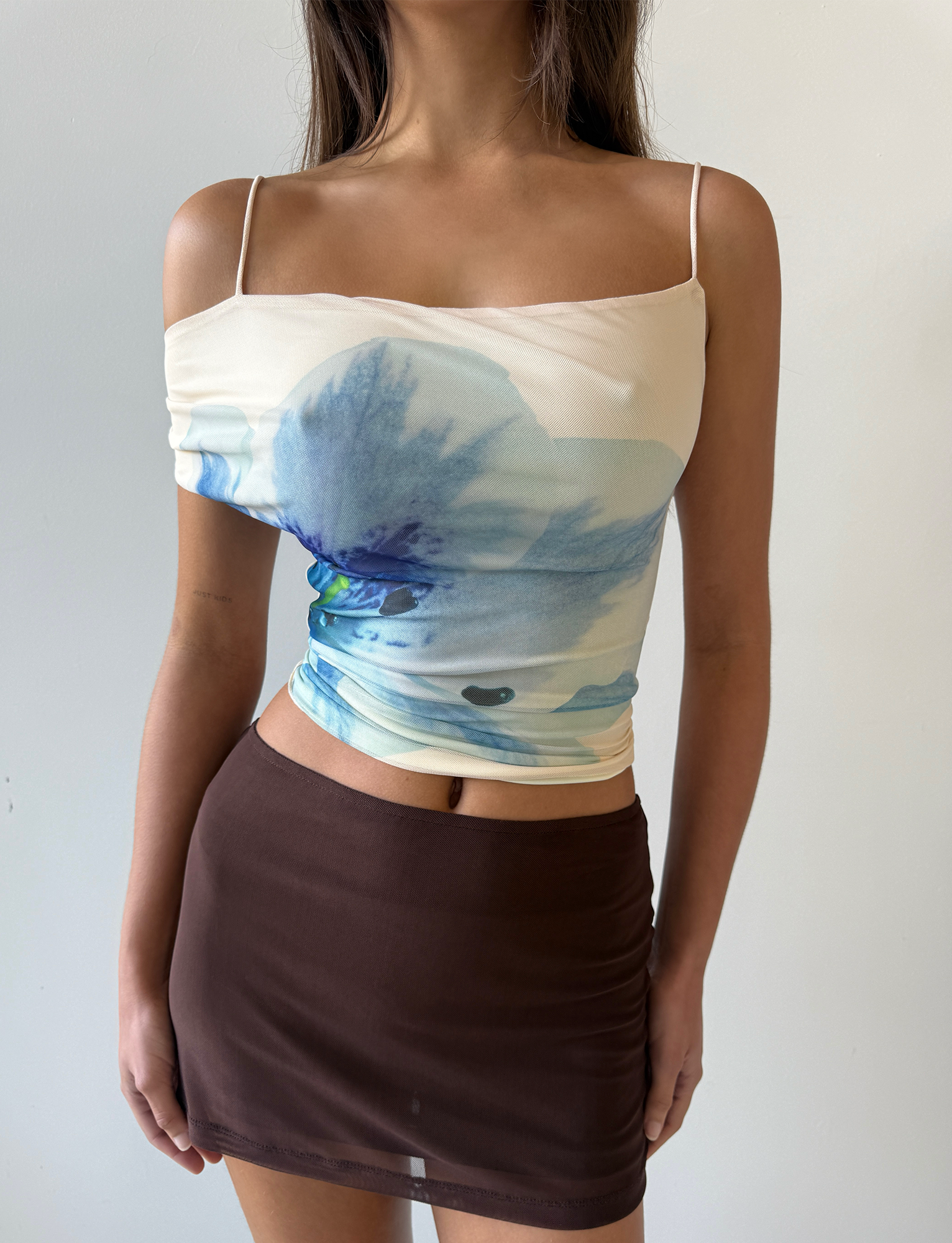 A woman wears the TIGERMIST LILLIAN TOP in cream floral with thin straps, paired with a fitted brown mini skirt, standing against a plain light background.