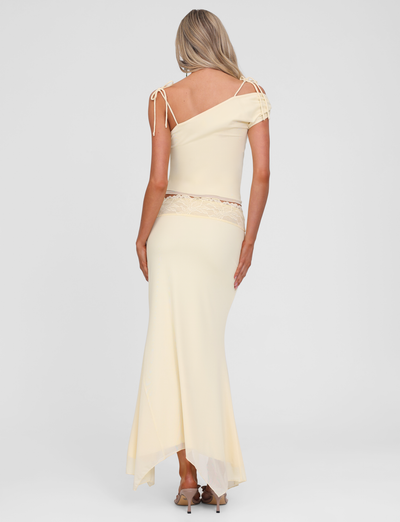 A woman with long blonde hair faces away, wearing the TIGERMIST LILLIAN SKIRT in yellow and beige heels, set against a plain white background.