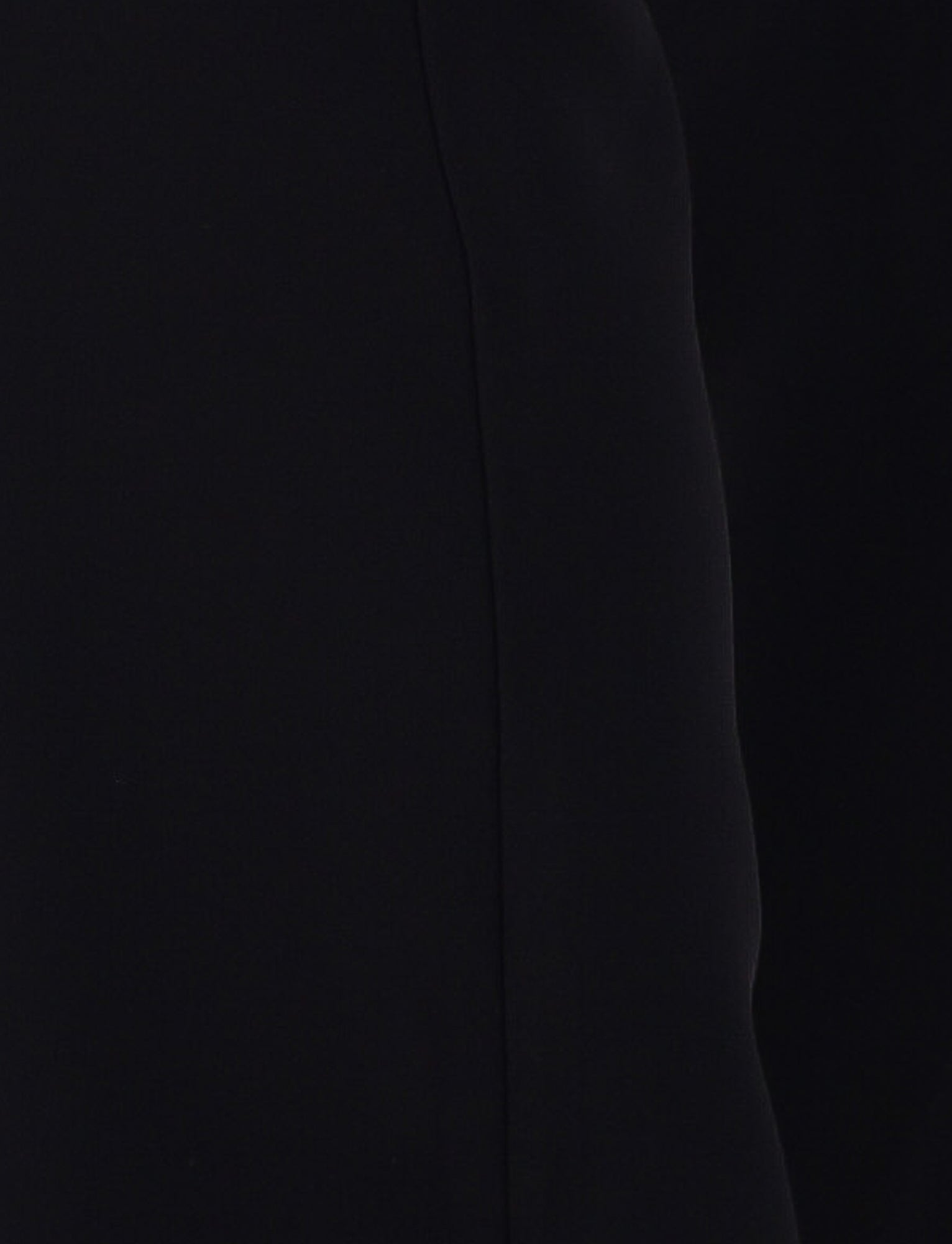 Close-up of the TERLA PANT - BLACK by TIGERMIST, showcasing its smooth, sleek black fabric with a vertical seam down the middle. The slightly curved fabric on the right side creates a subtle shadow effect, suggesting a flared silhouette.