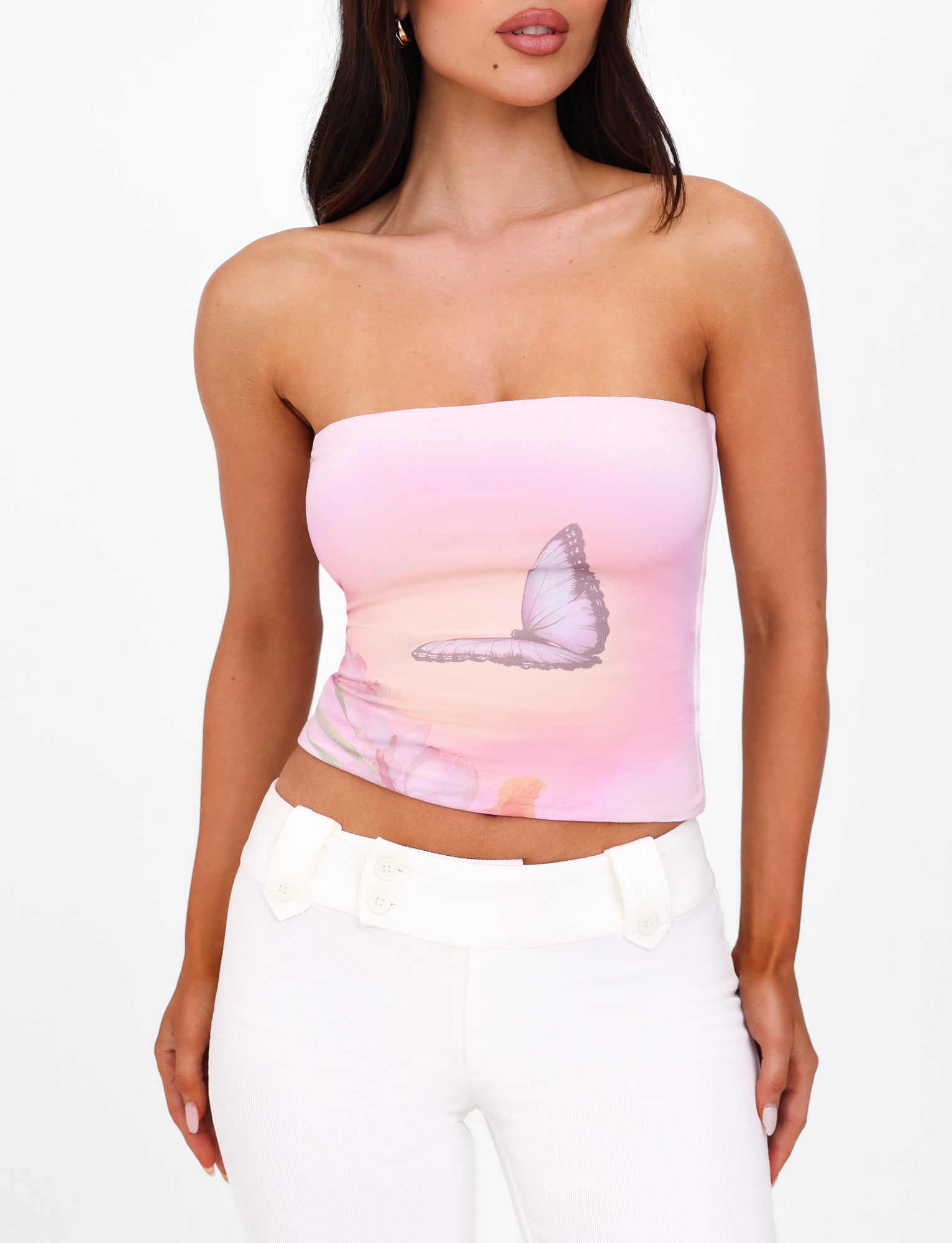 A woman is wearing the AMBROSE BOOB TUBE - PINK from TIGERMIST, paired with white pants. The background is plain white.