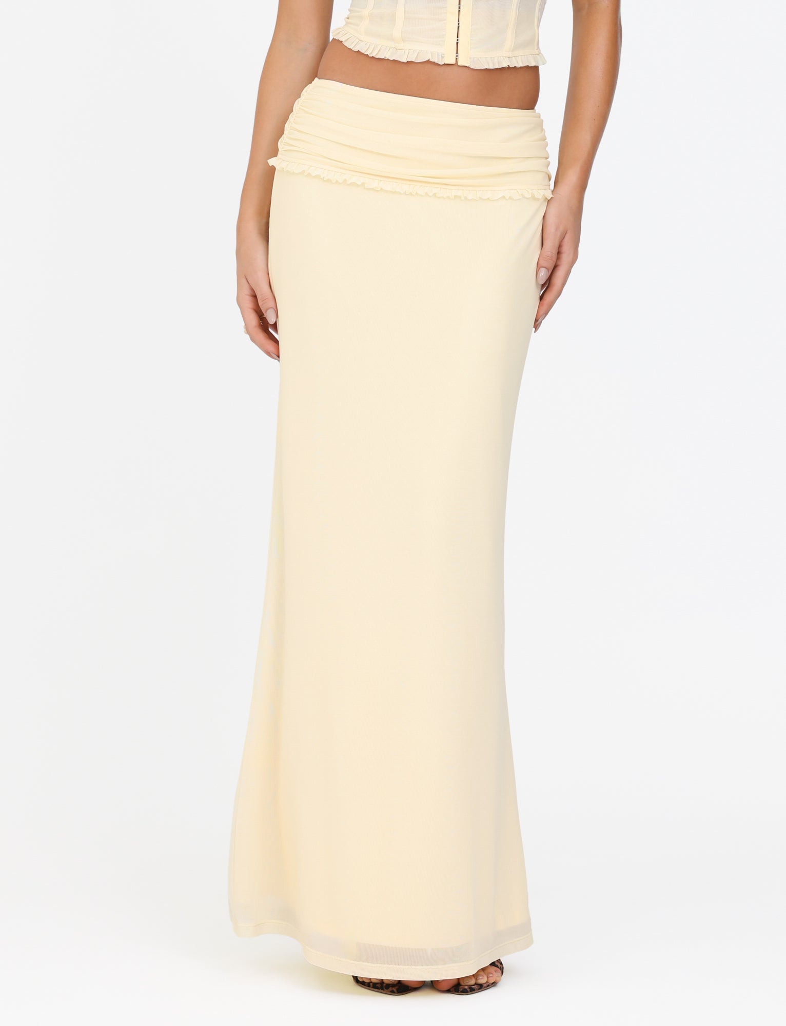 A person is wearing a lemon yellow Ginny Maxi Skirt by Tigermist, featuring a wide, ruched waistband, standing against a plain white background. Only the lower half of the body is elegantly draped in this floor-length maxi skirt.