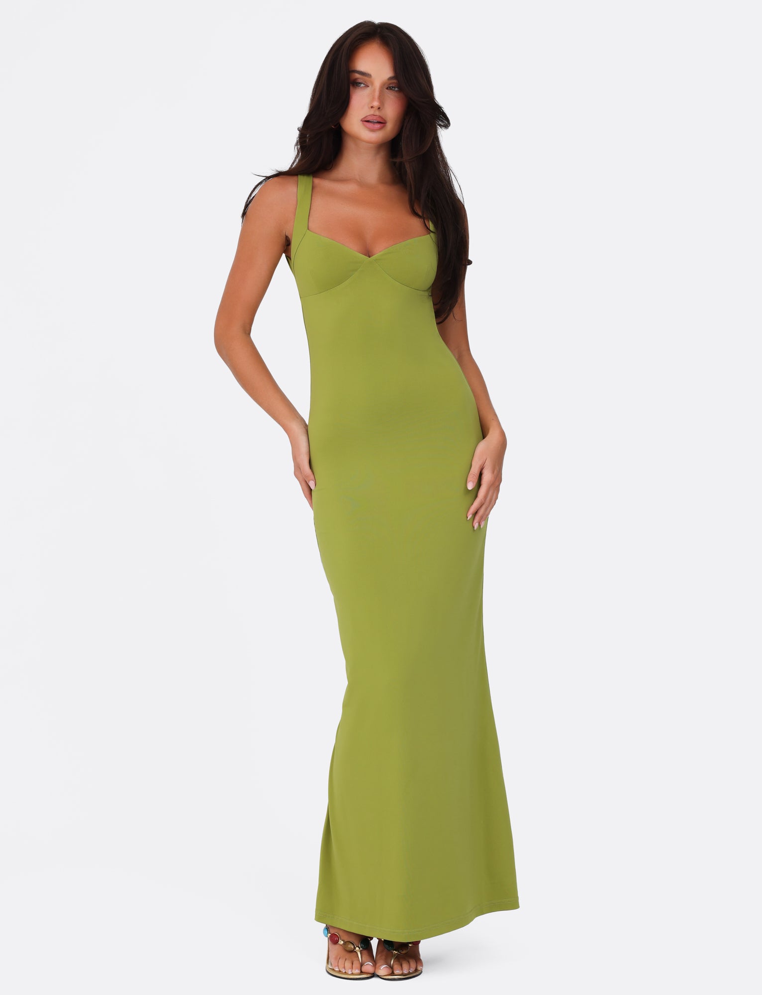 A person effortlessly strikes a pose wearing the SONNET MAXI DRESS - GREEN from TIGERMIST, set against a simple white background. The stunning, fitted maxi dress features a sweetheart neckline and gracefully extends to the floor. With long, dark hair cascading down their back, they exude confidence with one hand poised on their hip.